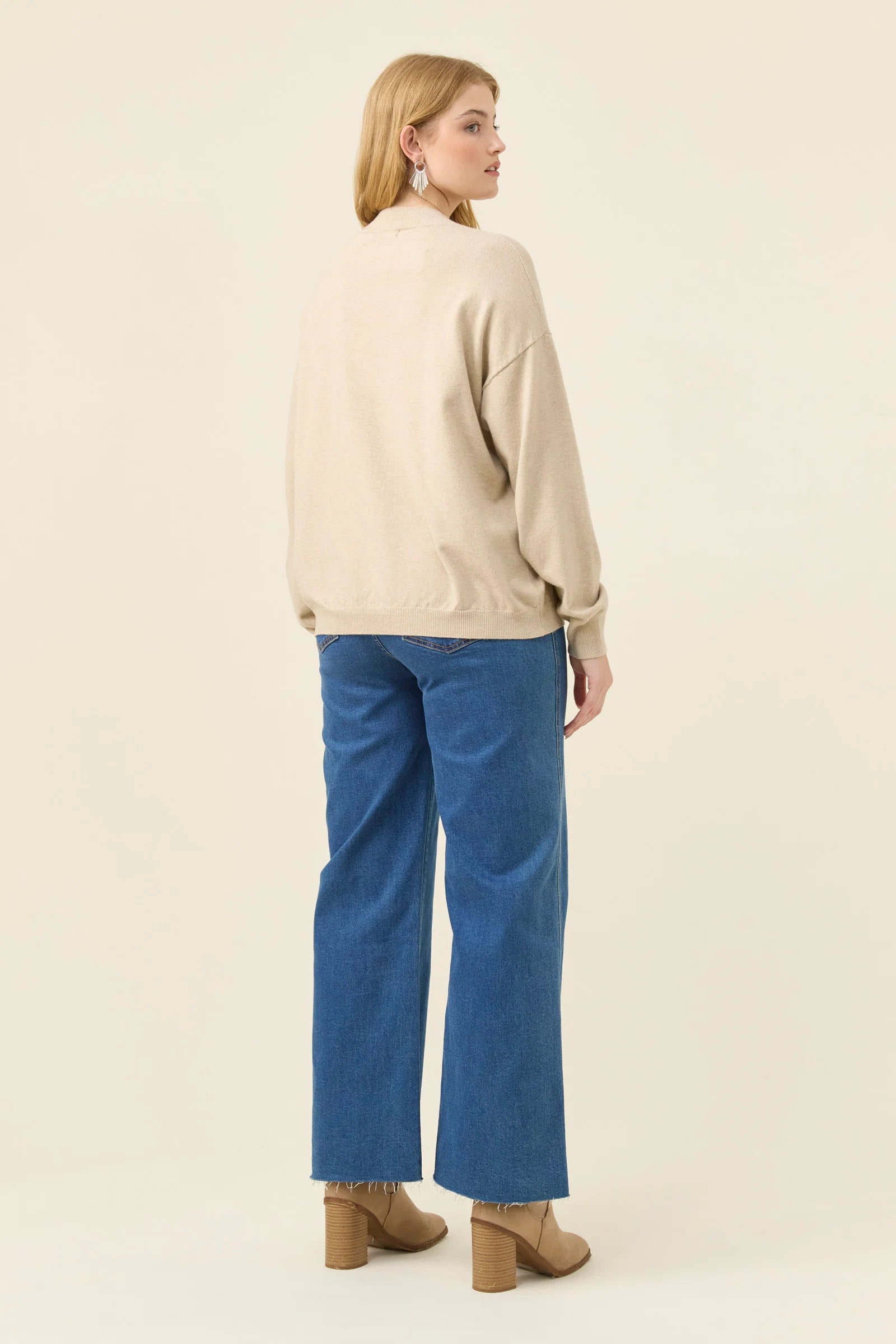 Image of Woman wearing a Isle of Mine beige sweater and blue jeans on a white background
