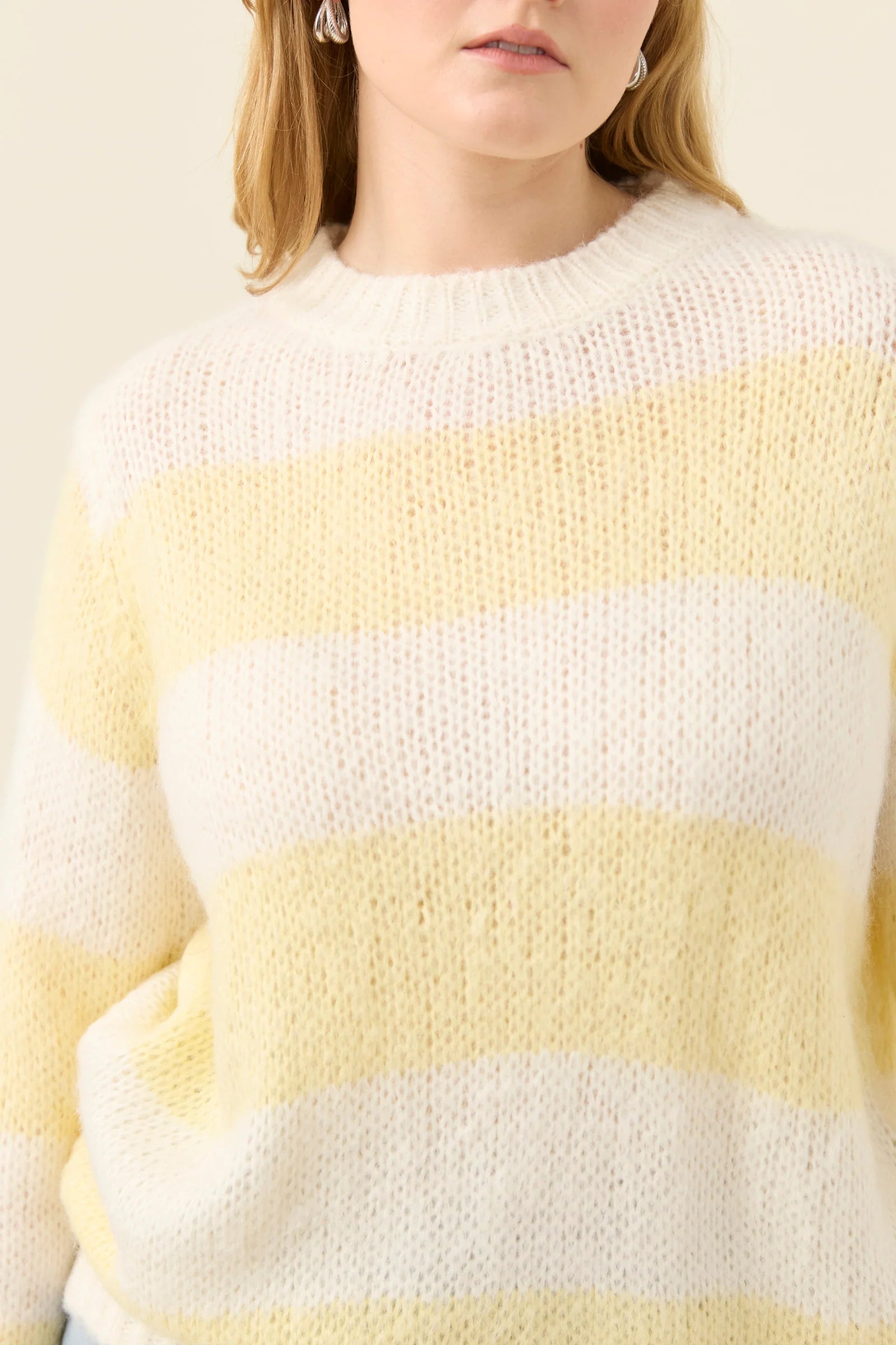 Woman wearing a Isle of Mine yellow and white striped sweater against a plain background