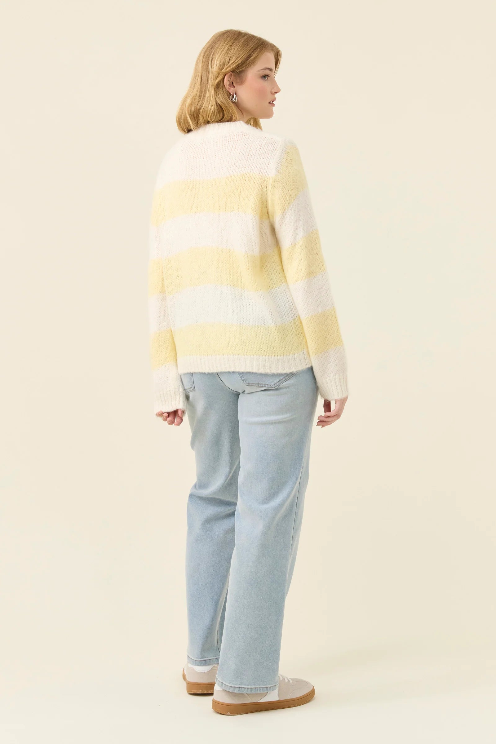 Woman wearing a Isle of Mine yellow and white striped sweater against a plain background