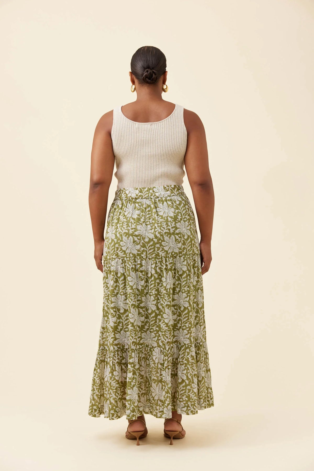 A woman shown from the back wearing a sleeveless cream ribbed knit top and a Isle of Mine long green floral maxi skirt, standing against a plain beige studio background.
