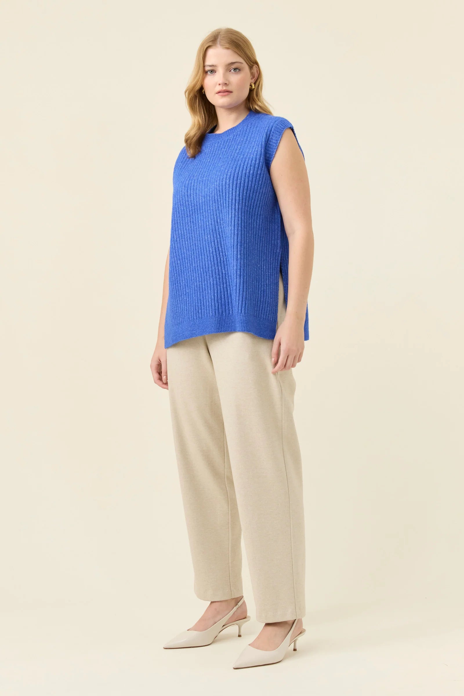 Image of Woman wearing a Isle of Mine blue sleeveless top and beige pants on a beige background