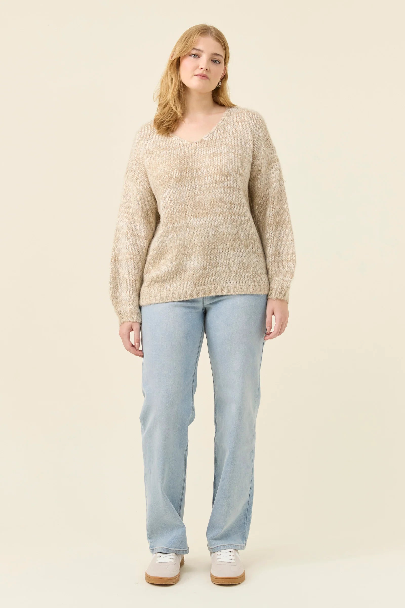 Woman wearing Isle of Mine knit in stone coloured. Paired with denim jeans on a plain background 
