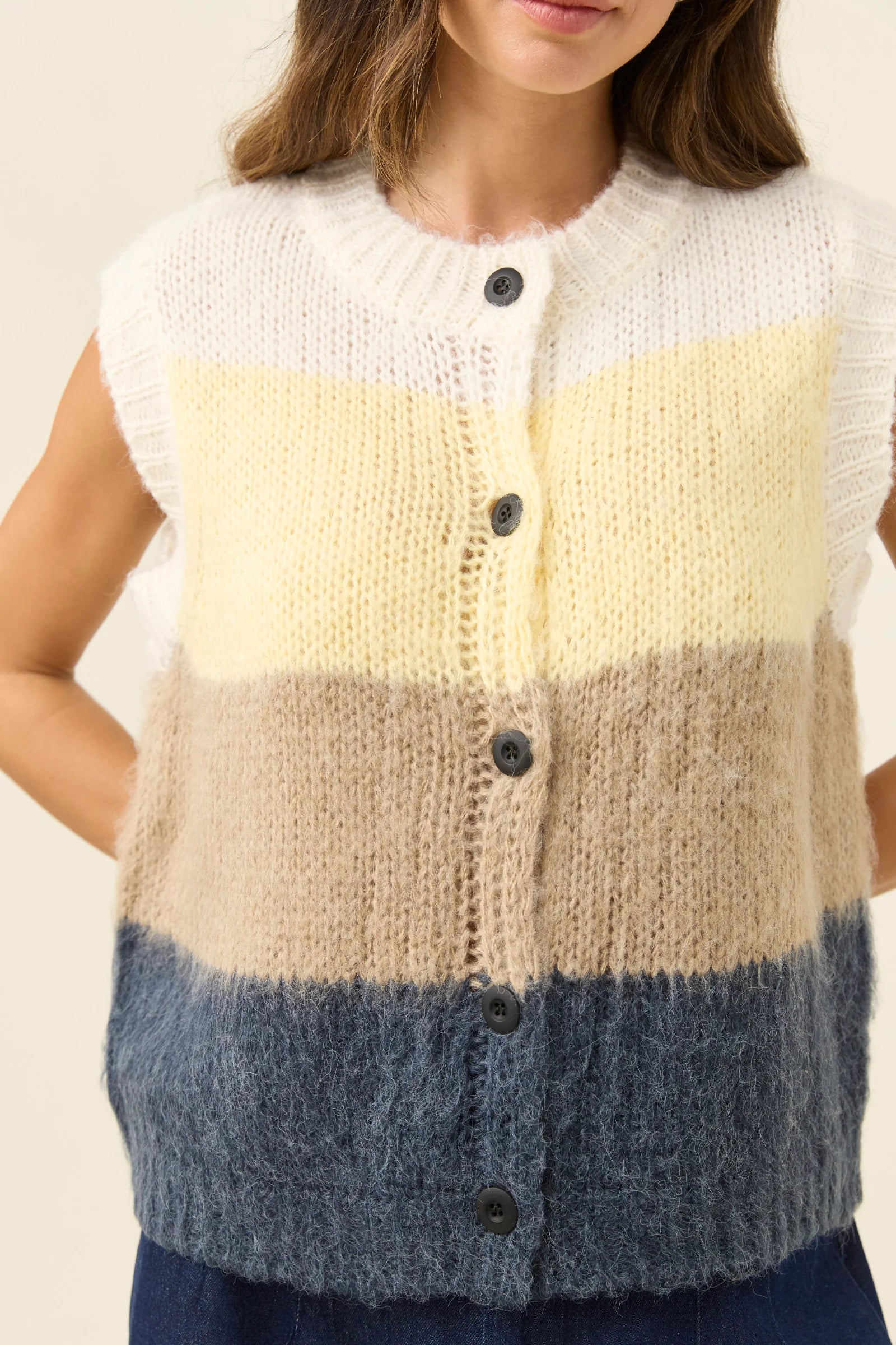 Woman wearing Isle of Mine Pallas Stripe Knit Vest in butter paired with denim jeans on a plain background 