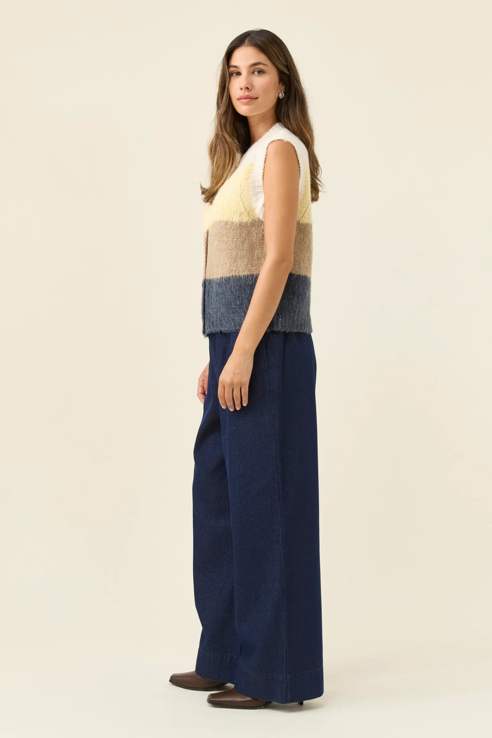 Image of Woman wearing Isle of Mine Pallas Stripe Knit Vest in butter paired with denim jeans on a plain background 