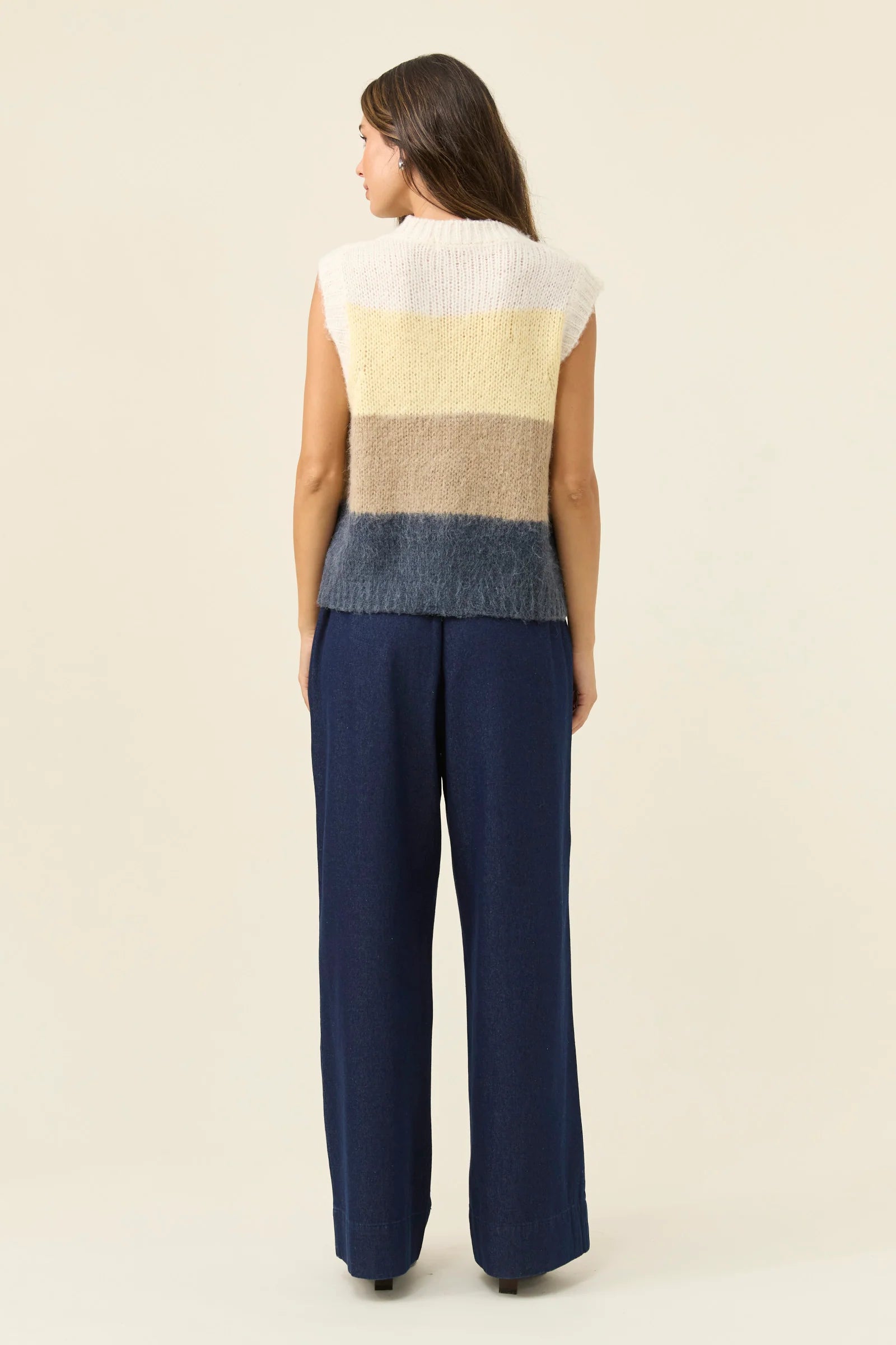 Image of Woman wearing Isle of Mine Pallas Stripe Knit Vest in butter paired with denim jeans on a plain background 