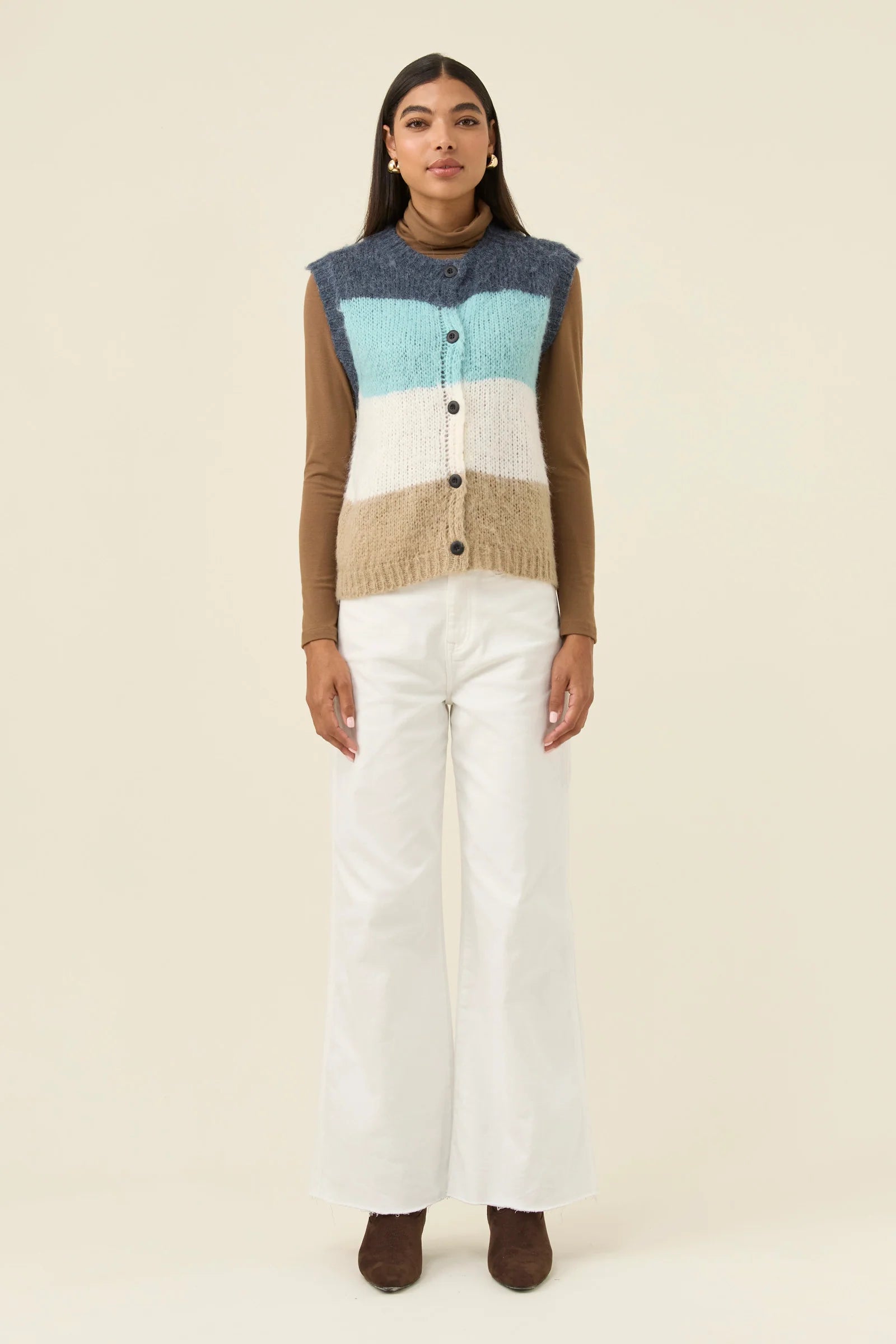 Woman wearing Isle of Mine knitted vest paired with white denim jeans on a plain background