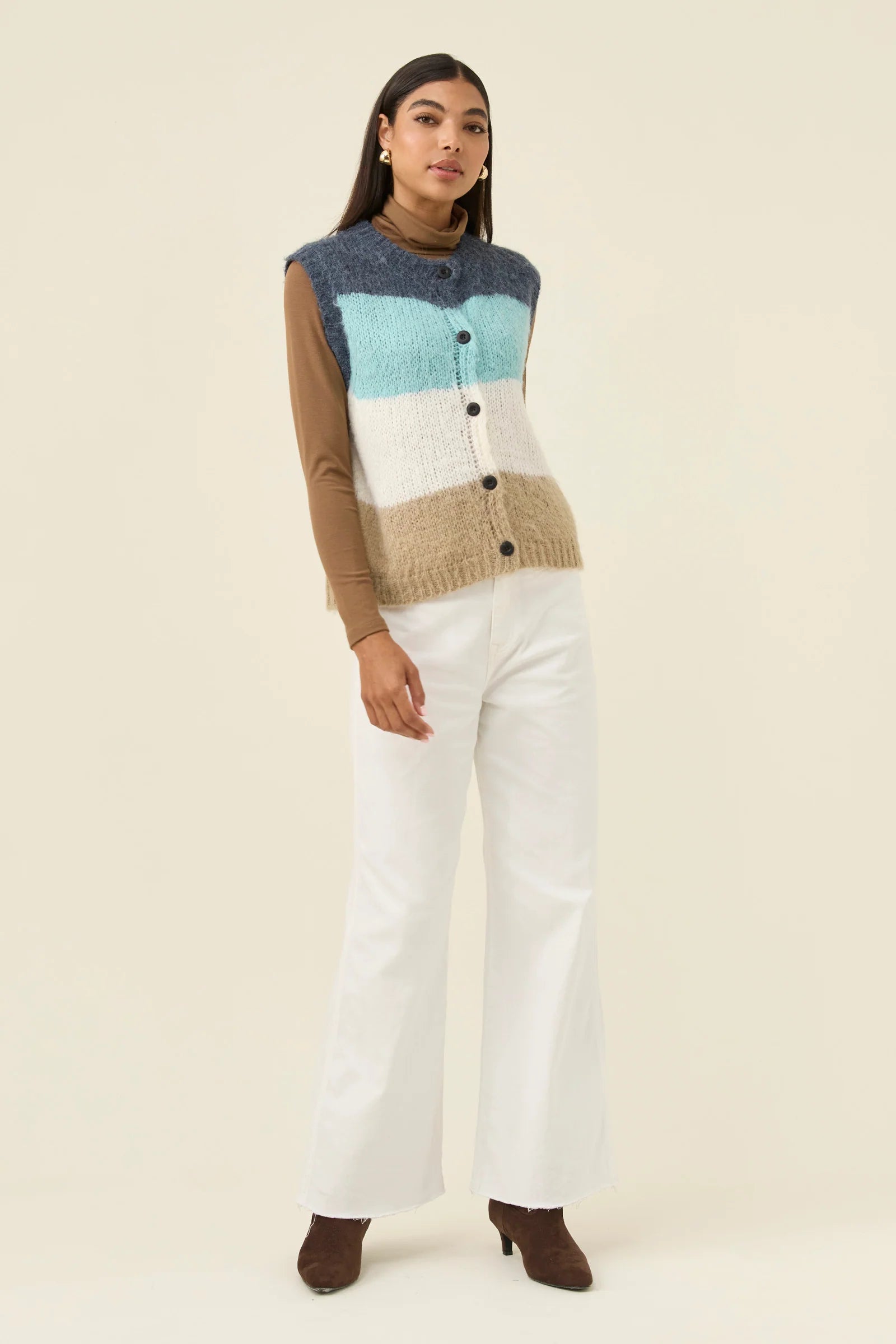 Image of Woman wearing Isle of Mine knitted vest paired with white denim jeans on a plain background