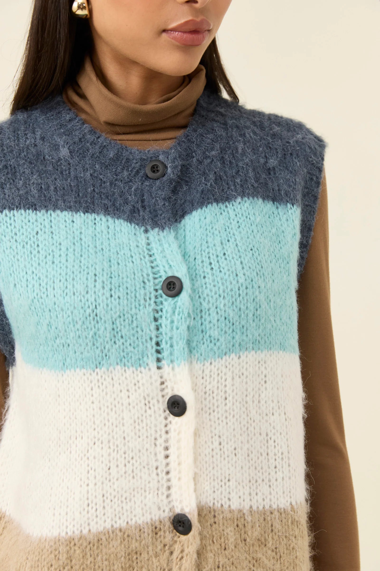 Woman wearing Isle of Mine knitted vest paired with white denim jeans on a plain background