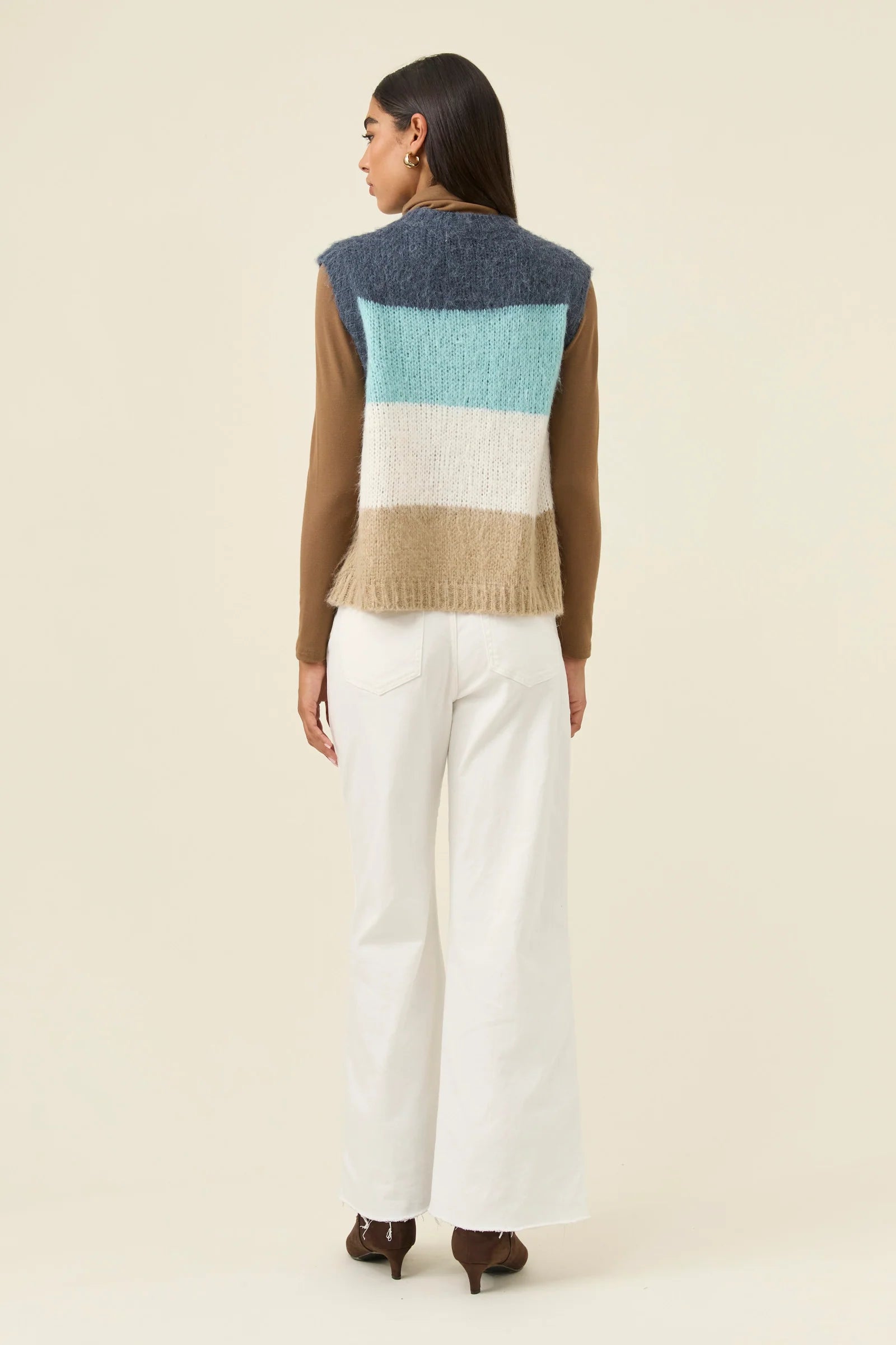 Woman wearing Isle of Mine knitted vest paired with white denim jeans on a plain background