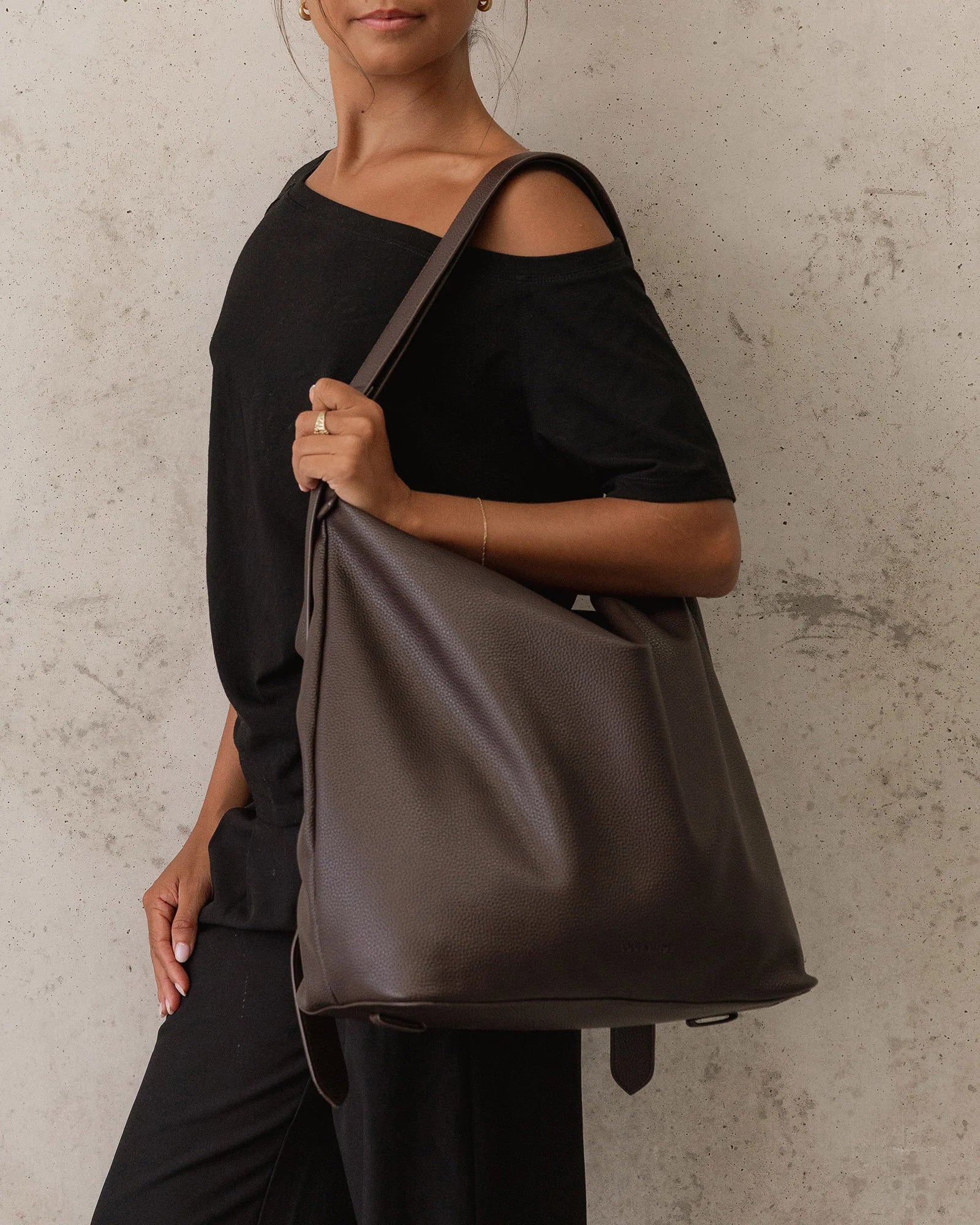 Image of Woman holding a Louenhide brown leather bag against a neutral background