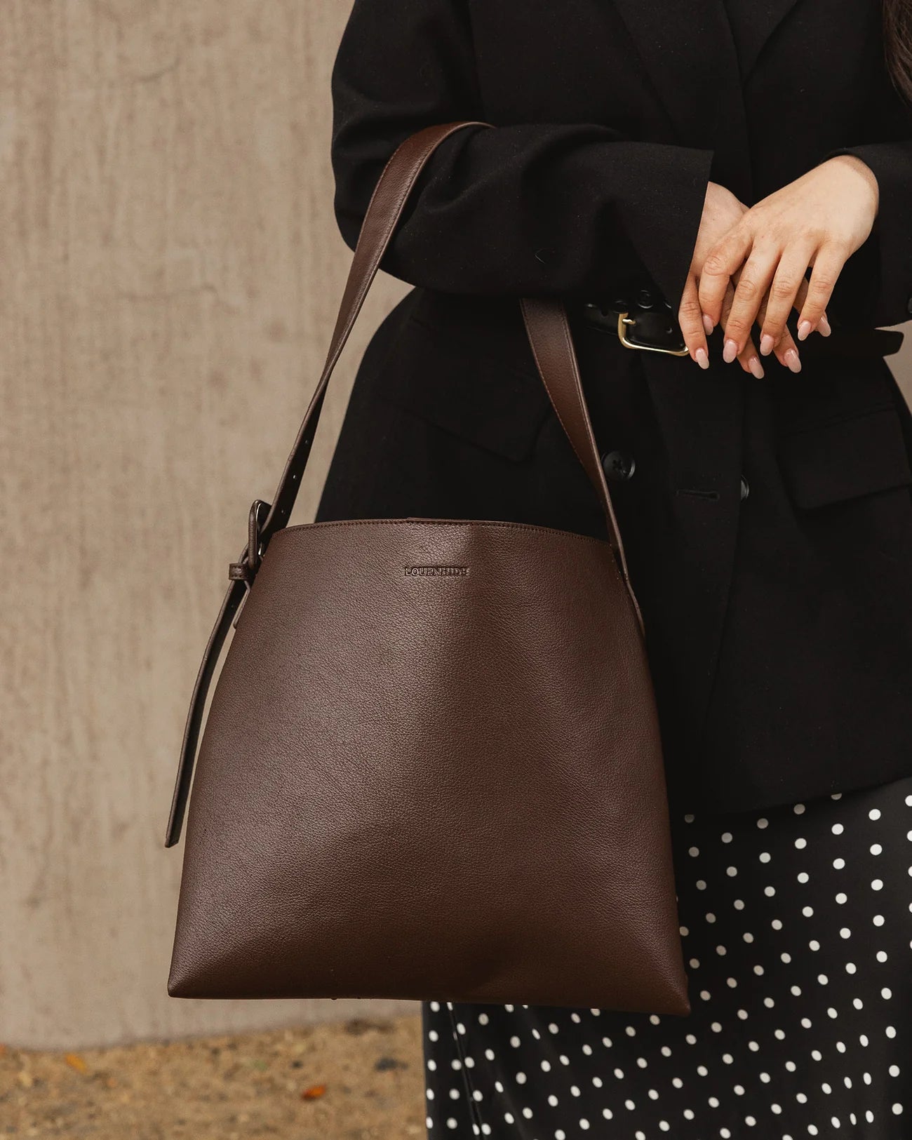 Woman holding a brown leather Louenhide bag with a neutral background