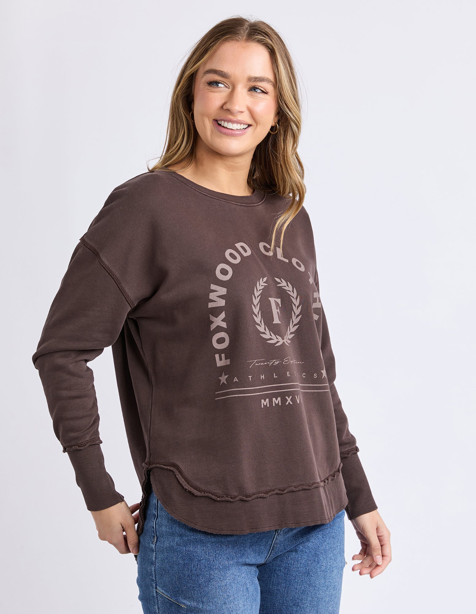 Image of Woman wearing a brown Foxwood jumper with a logo and text on a white background