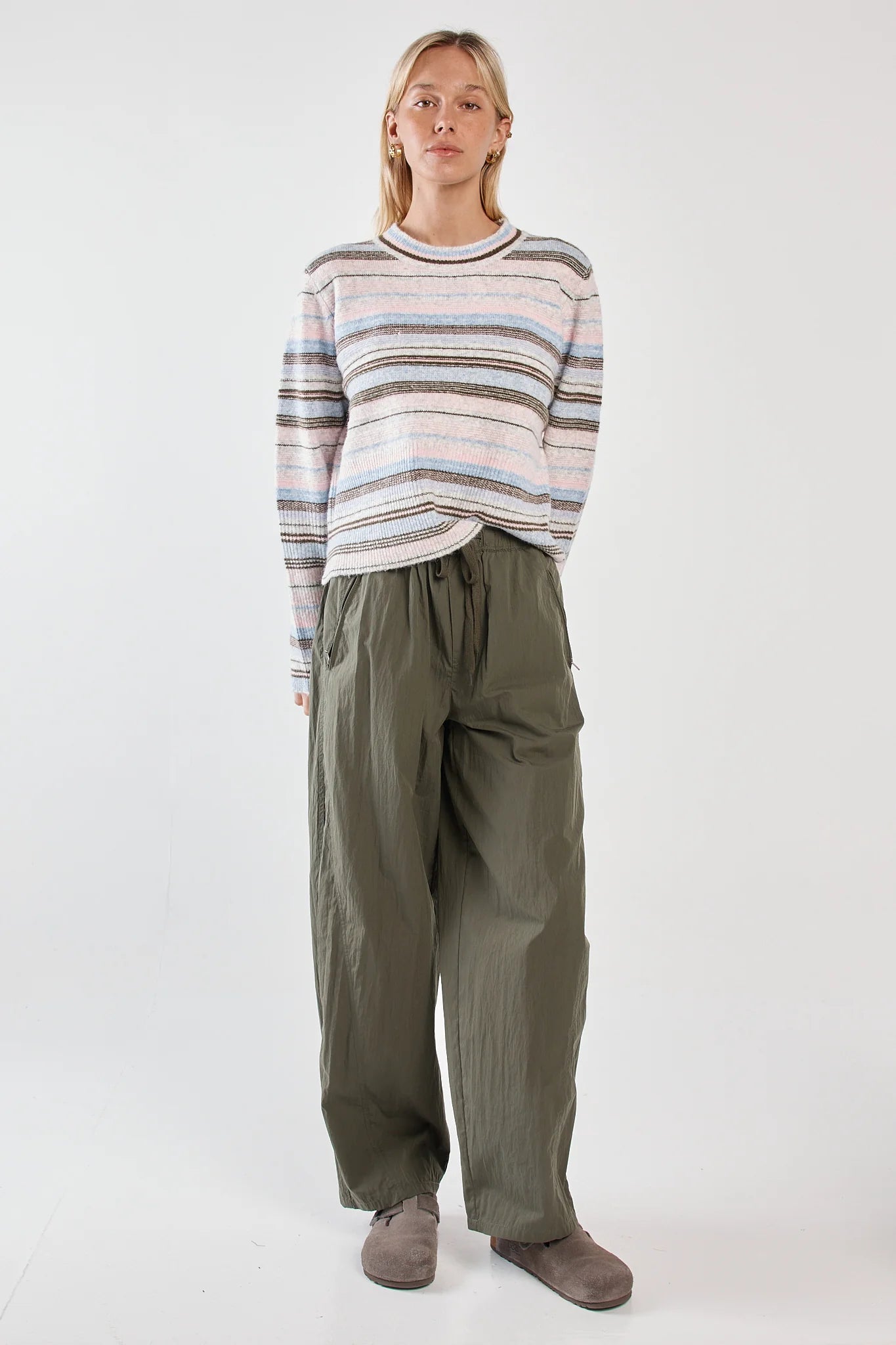 Woman wearing a striped sweater and green pants on a white background
