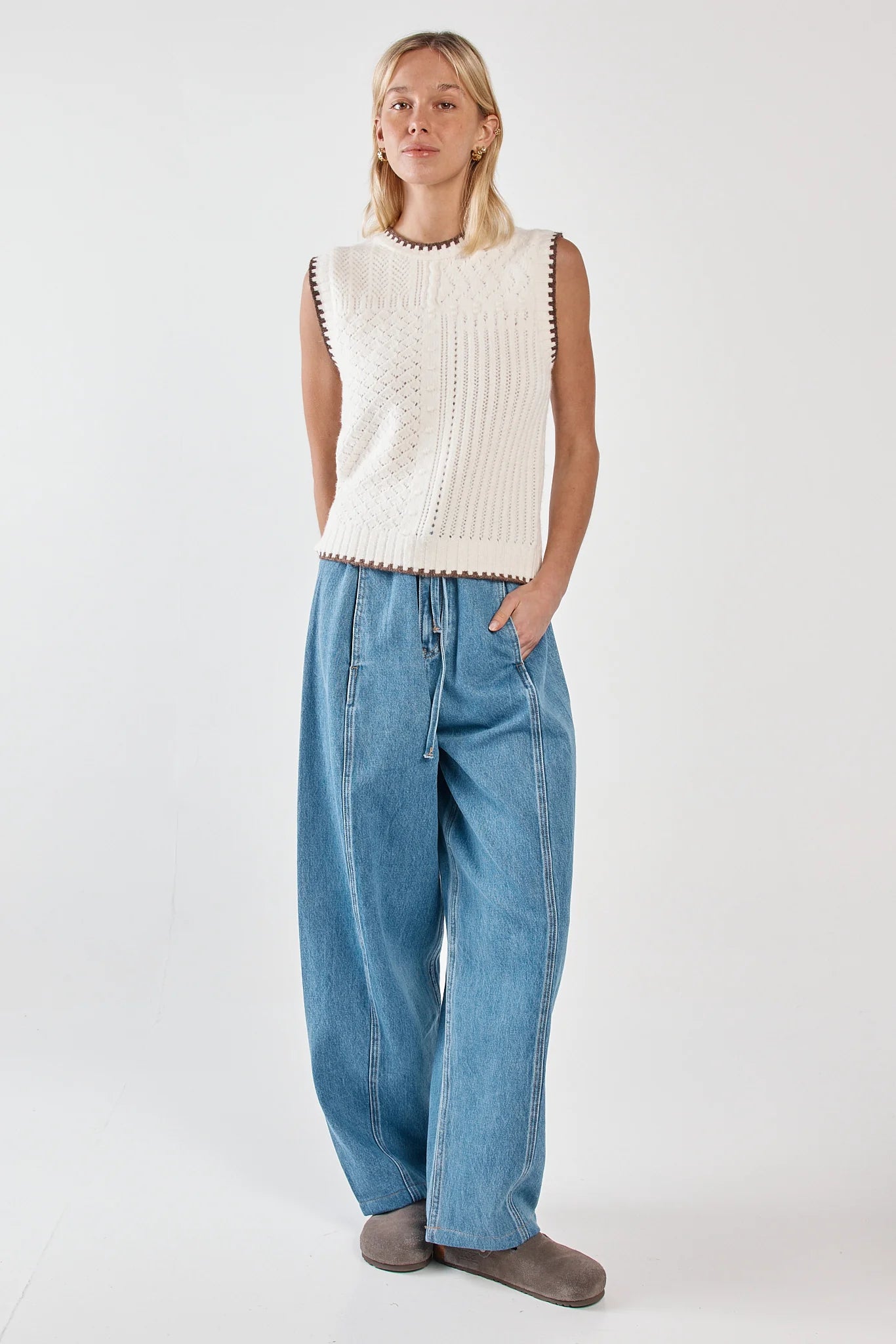 Image of Woman wearing a white sleeveless knitted top and Sass blue jeans on a white background