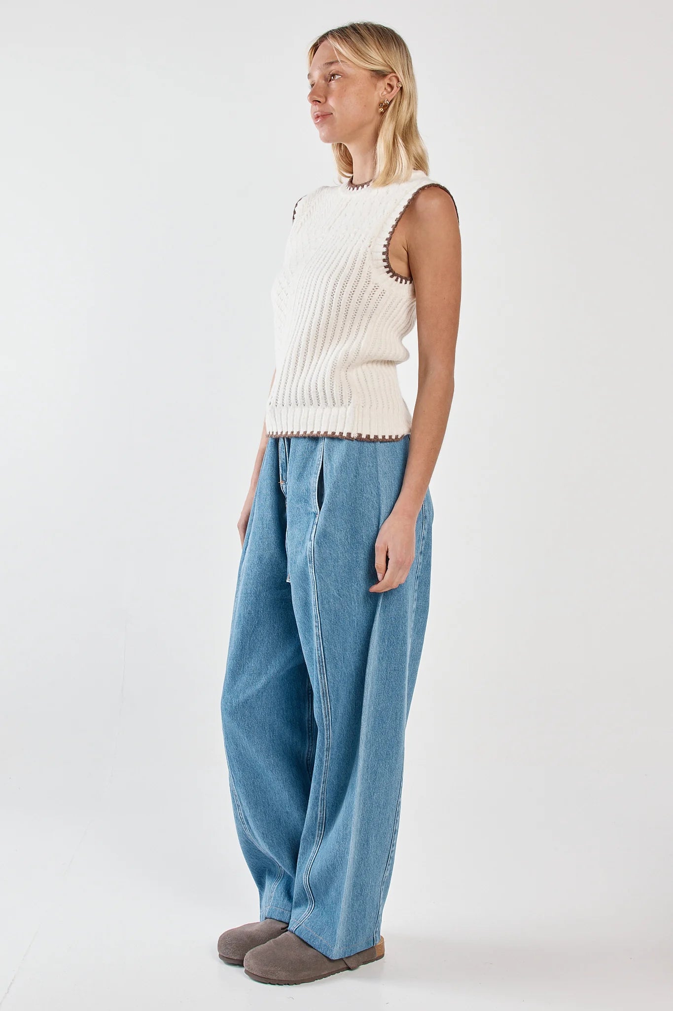 Woman wearing a cream sleeveless sweater and Sass blue pants on a white background