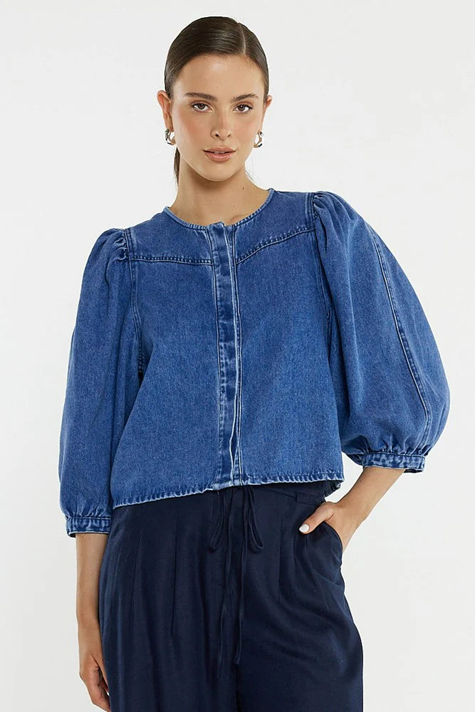 Woman wearing a Sass blue denim blouse with puffed sleeves on a white background