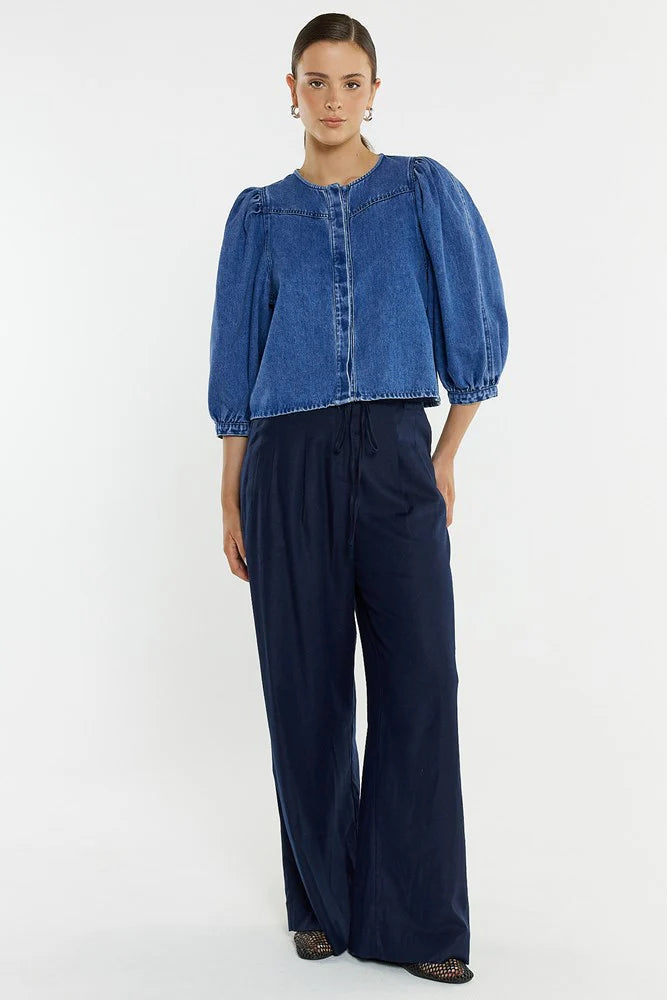 Woman wearing a Sass blue denim top and navy pants on a white background