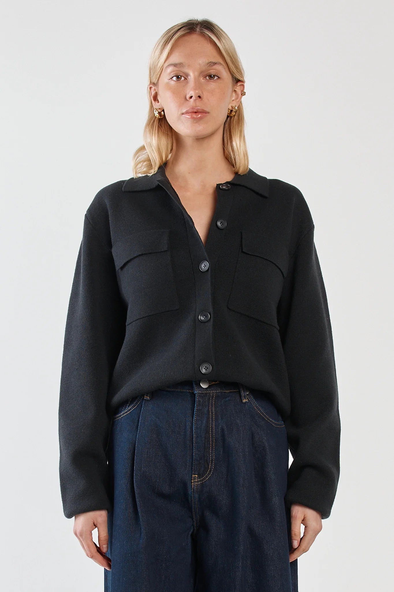 Woman wearing a Sass black button-up jacket and dark jeans on a white background