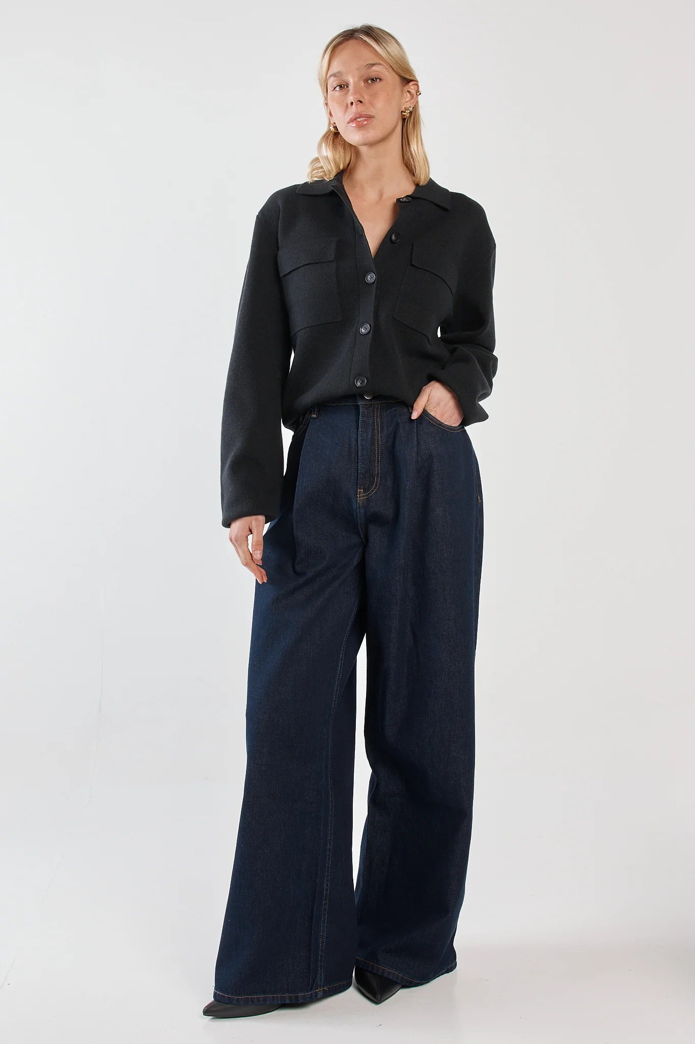 Image of Woman wearing a Sass black jacket and dark blue pants on a white background
