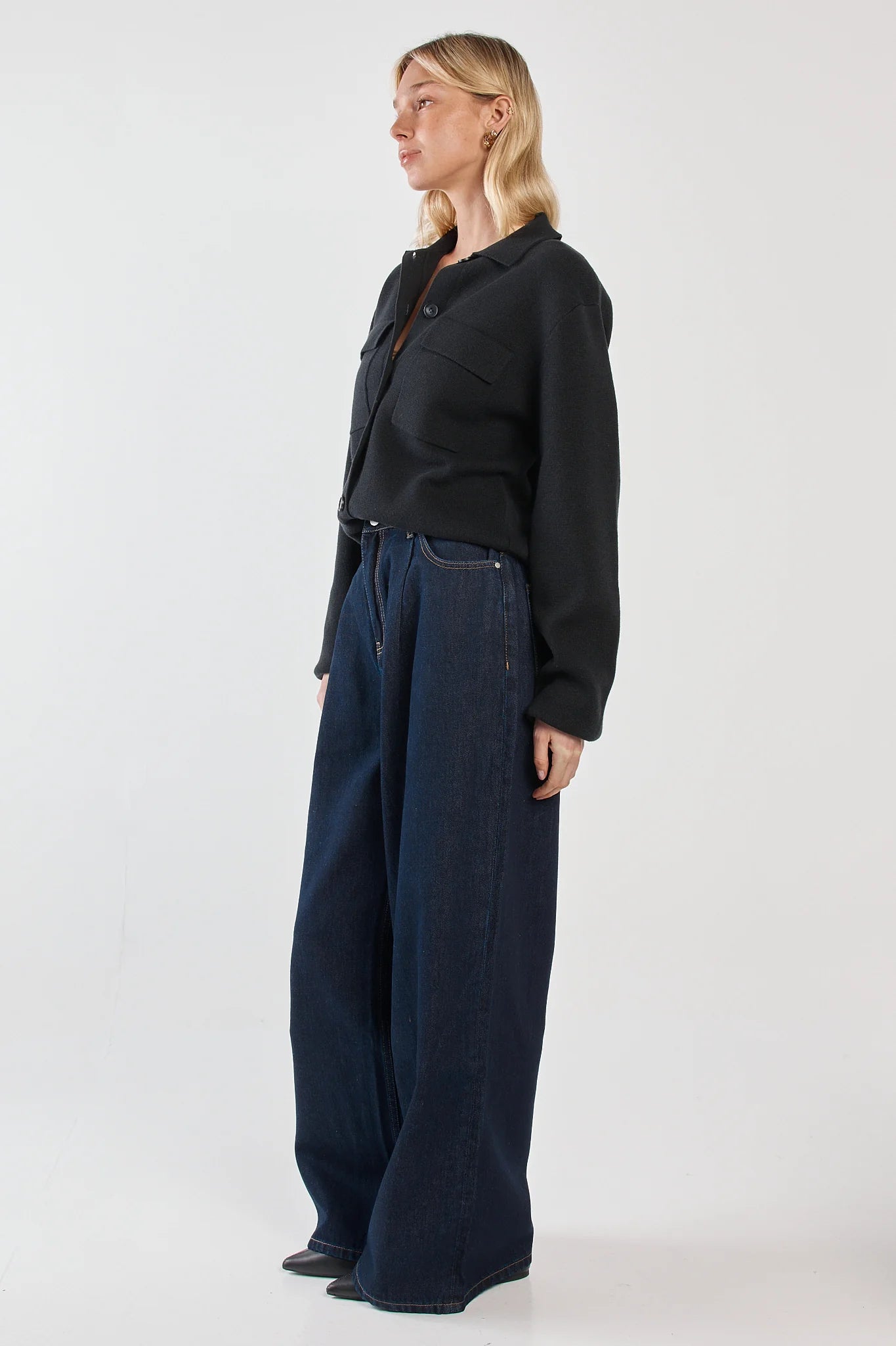 Woman wearing a Sass black jacket and blue jeans on a white background