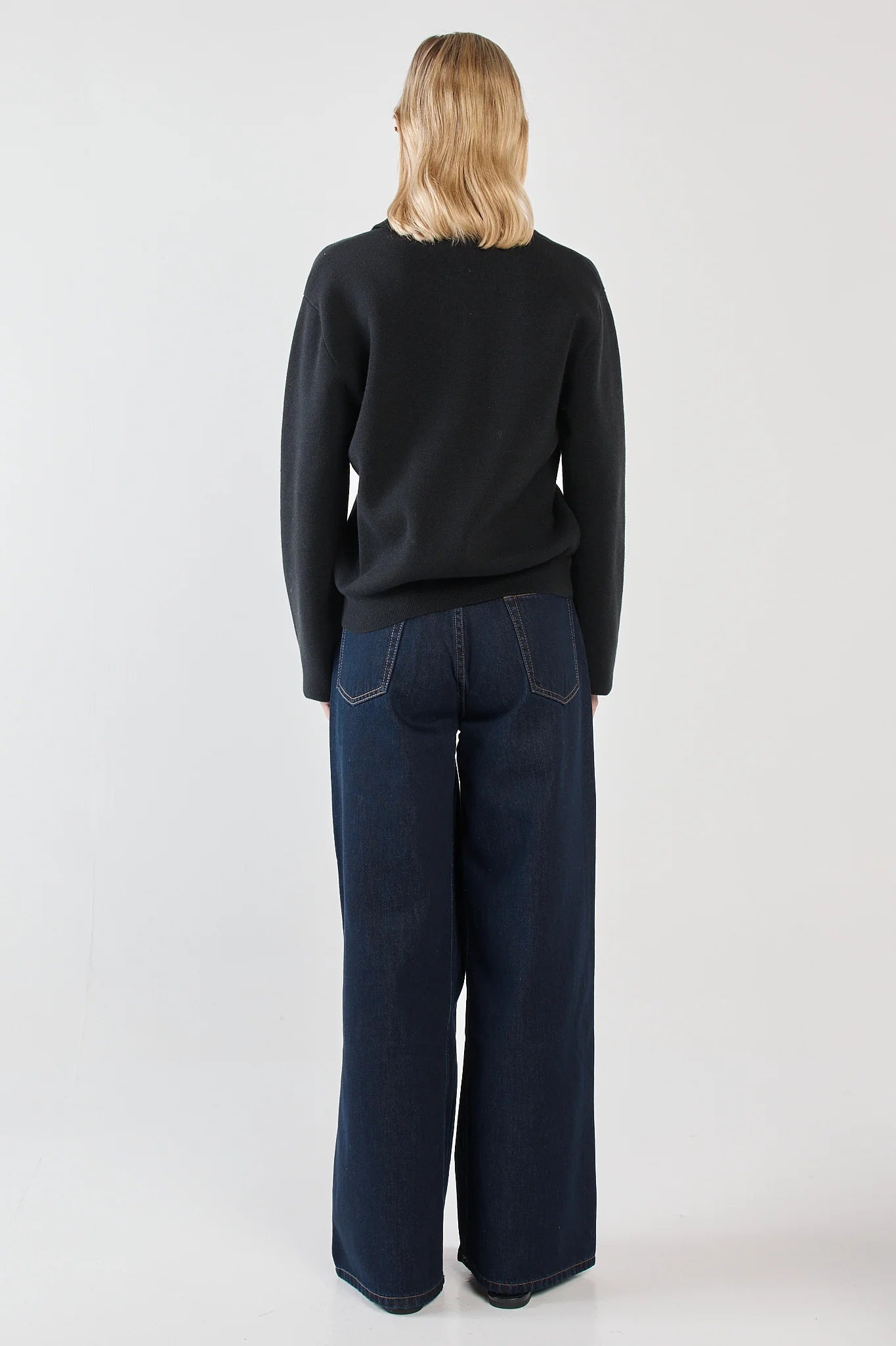 Woman wearing a Sass black sweater and blue jeans on a white background