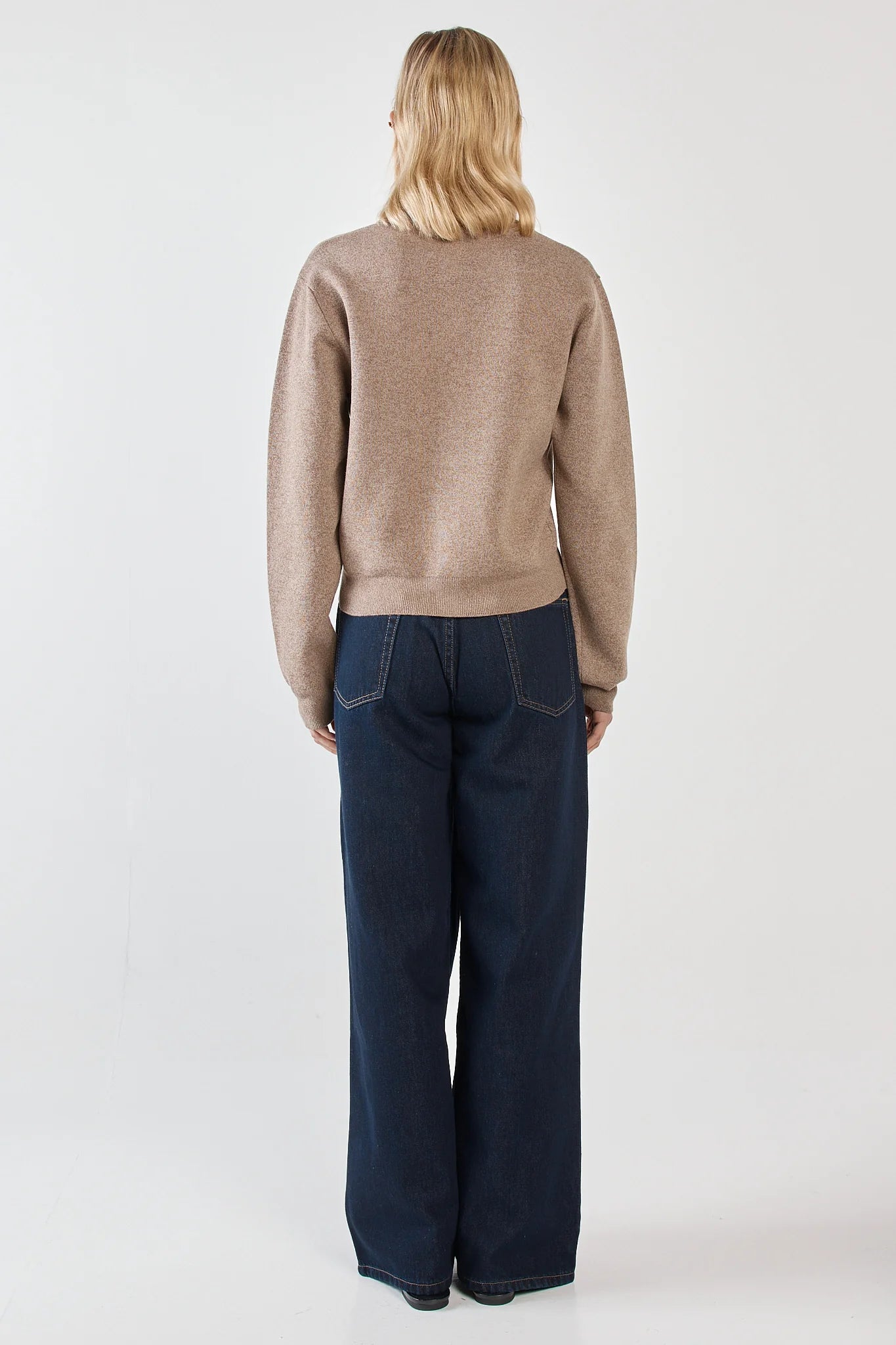 Image of Woman wearing a Sass beige sweater and dark blue jeans on a white background