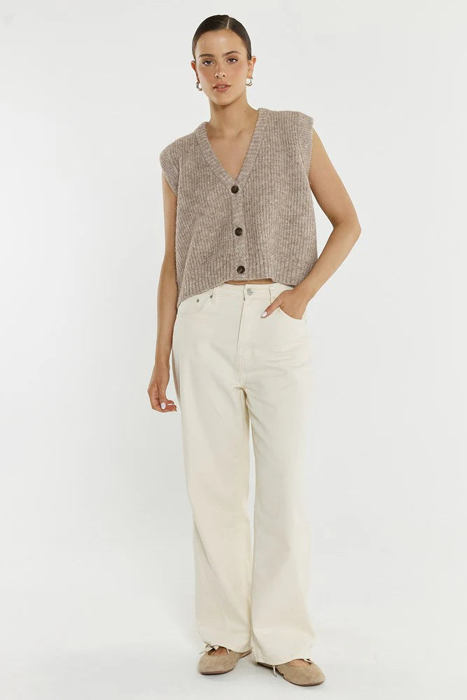 Woman wearing a Sass beige knitted vest and white pants on a white background