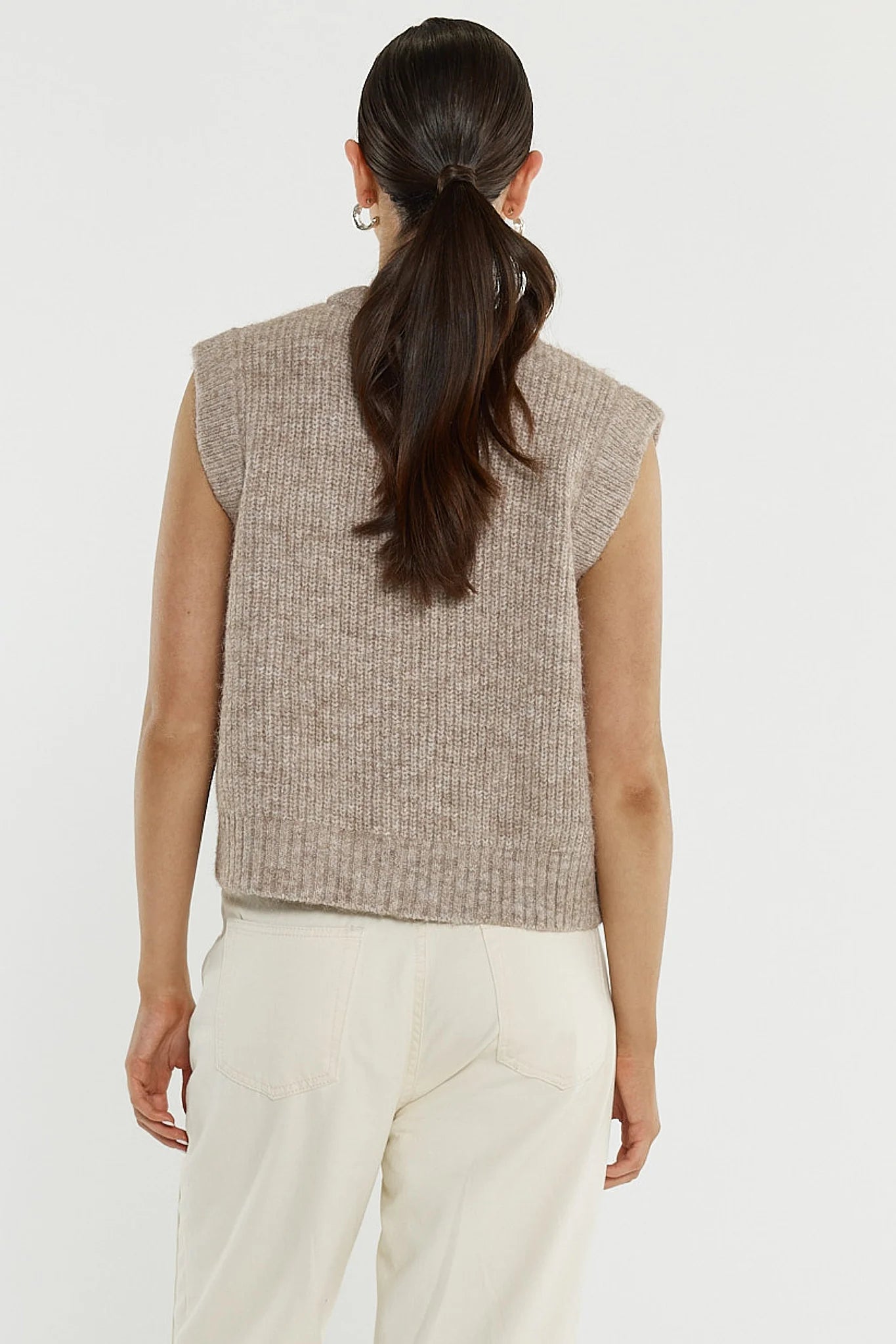 Woman wearing a Sass sleeveless knitted top and white pants on a plain background