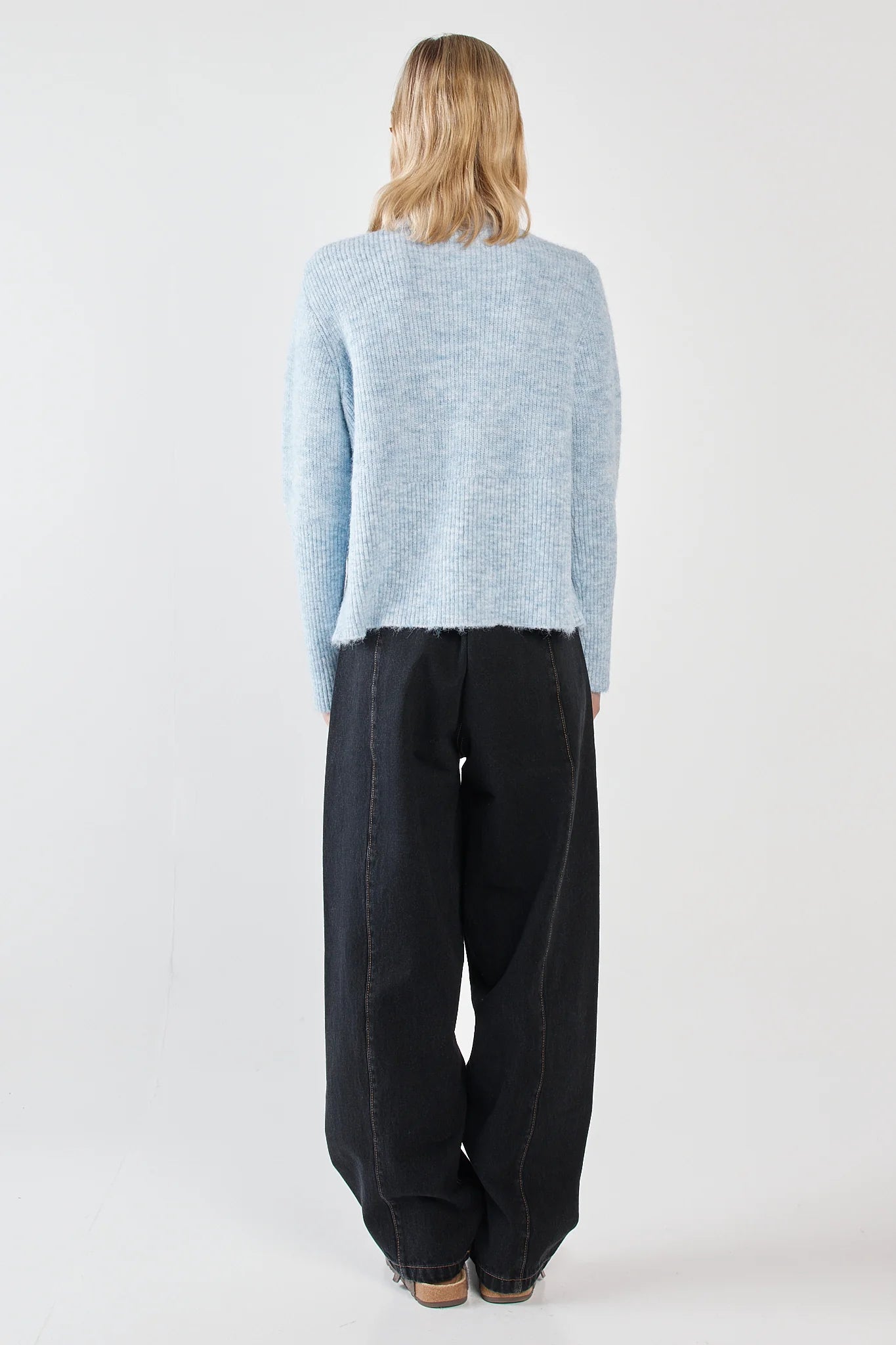 Image of Woman wearing a Sass light blue sweater and dark pants on a white background