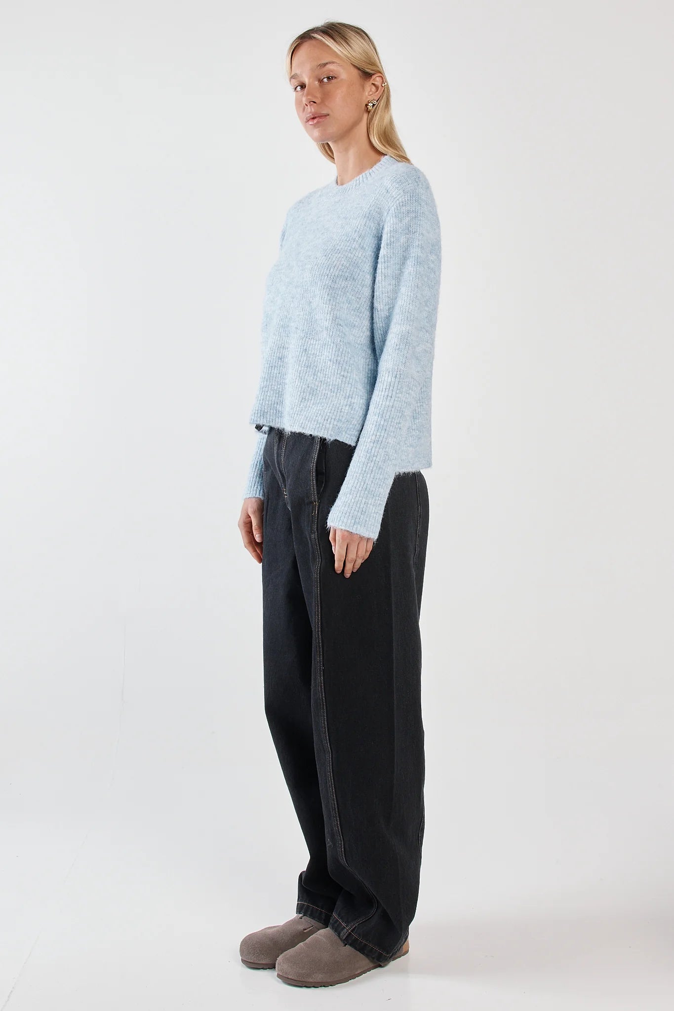 Woman wearing a Sass light blue sweater and black pants on a white background