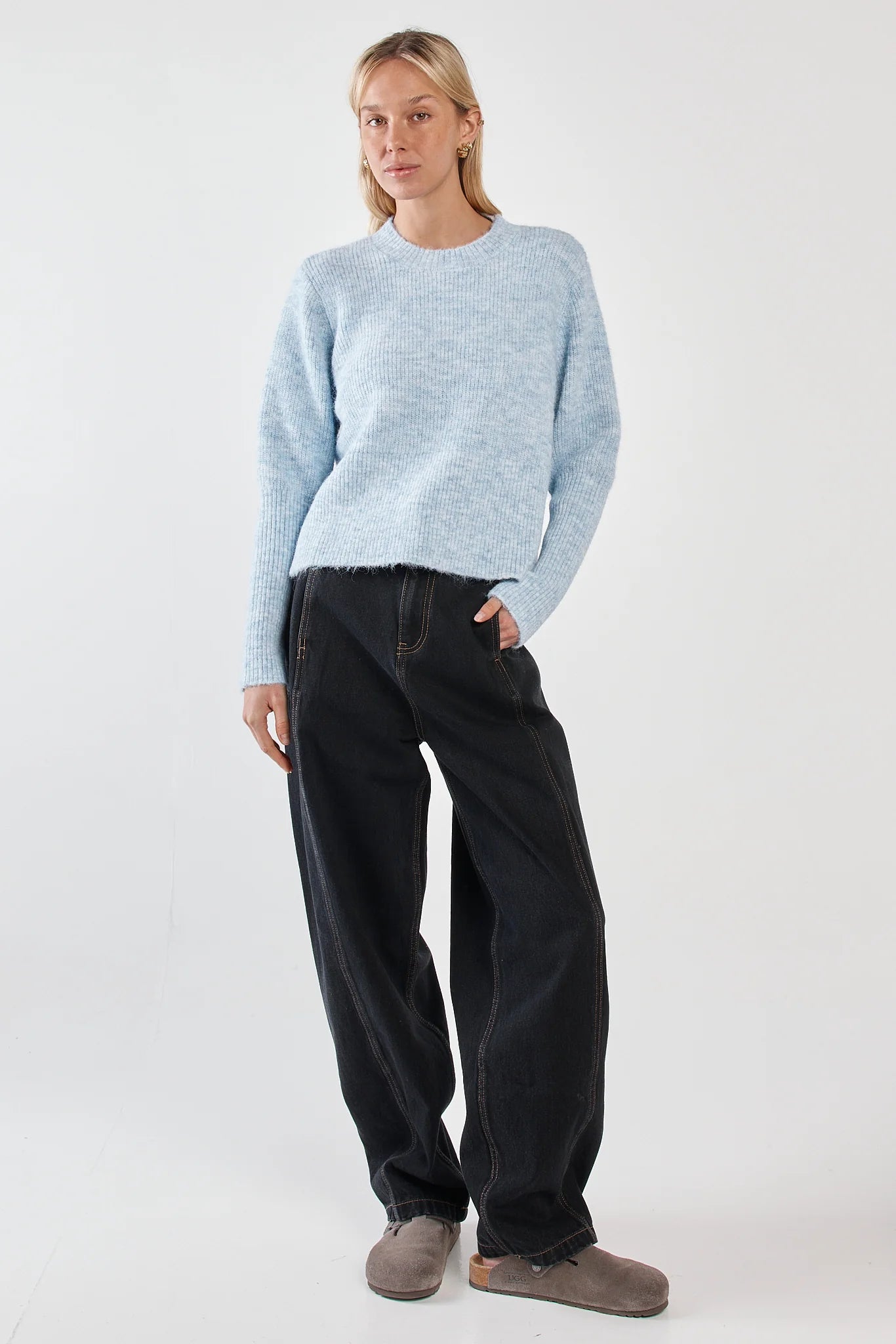 Woman wearing a Sass light blue sweater and black pants on a white background