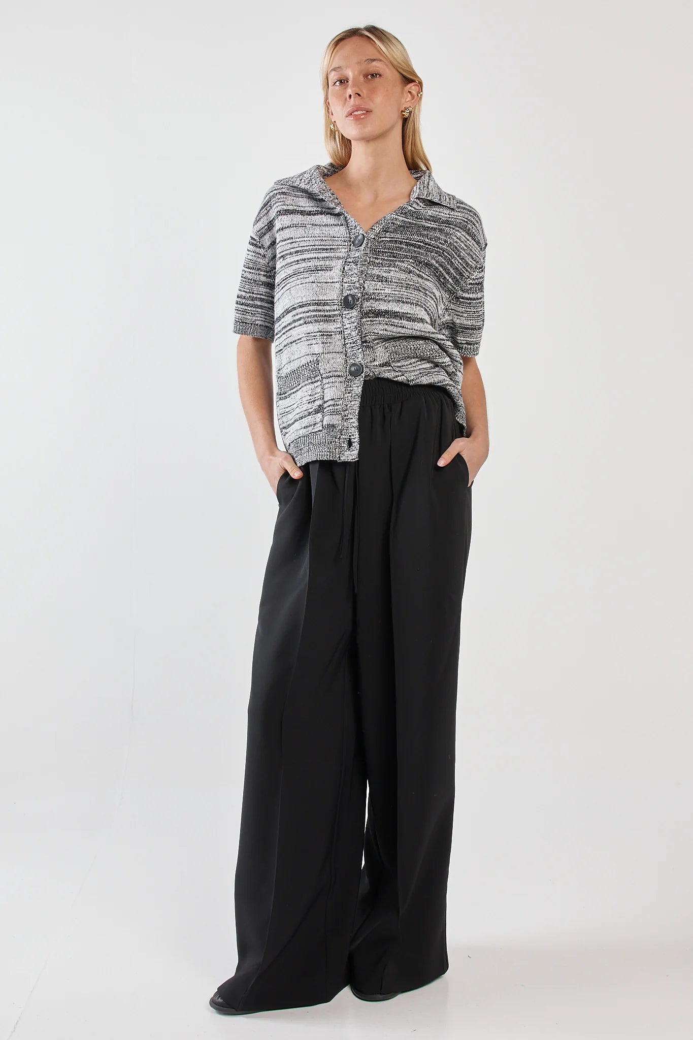 Woman wearing a patterned cardigan and Sass black pants on a white background