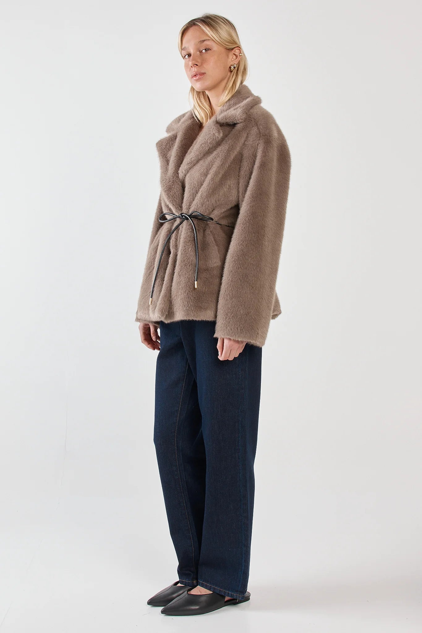 Woman wearing a Sass brown coat and dark blue pants on a white background