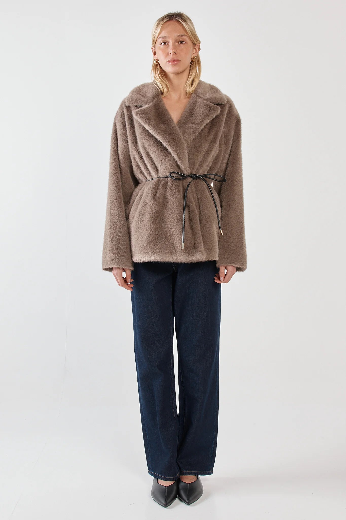 Woman wearing a sass brown coat and navy pants on a white background