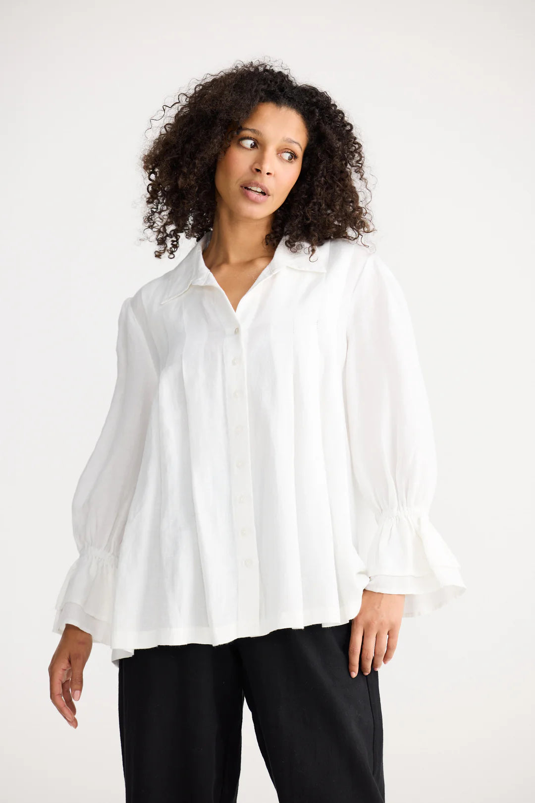 Woman wearing a Shanty Corporation white blouse and black pants on a white background