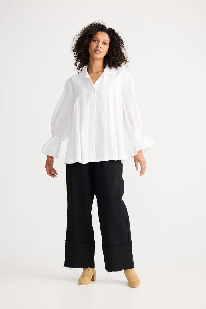 Woman wearing a Shanty Corporation white blouse and black pants on a white background