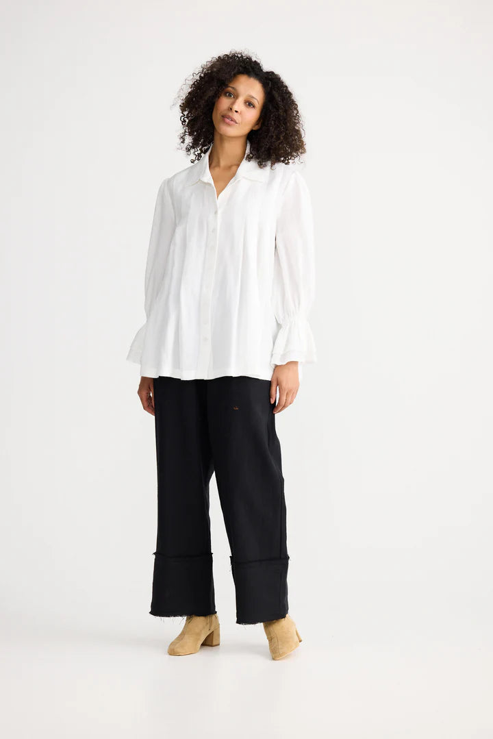 Woman wearing a Shanty Corporation white blouse and black pants on a white background