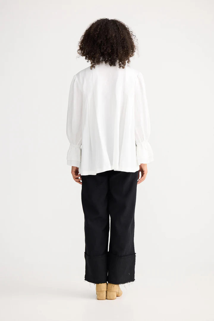 Woman wearing a Shanty Corporation white blouse and black pants on a white background