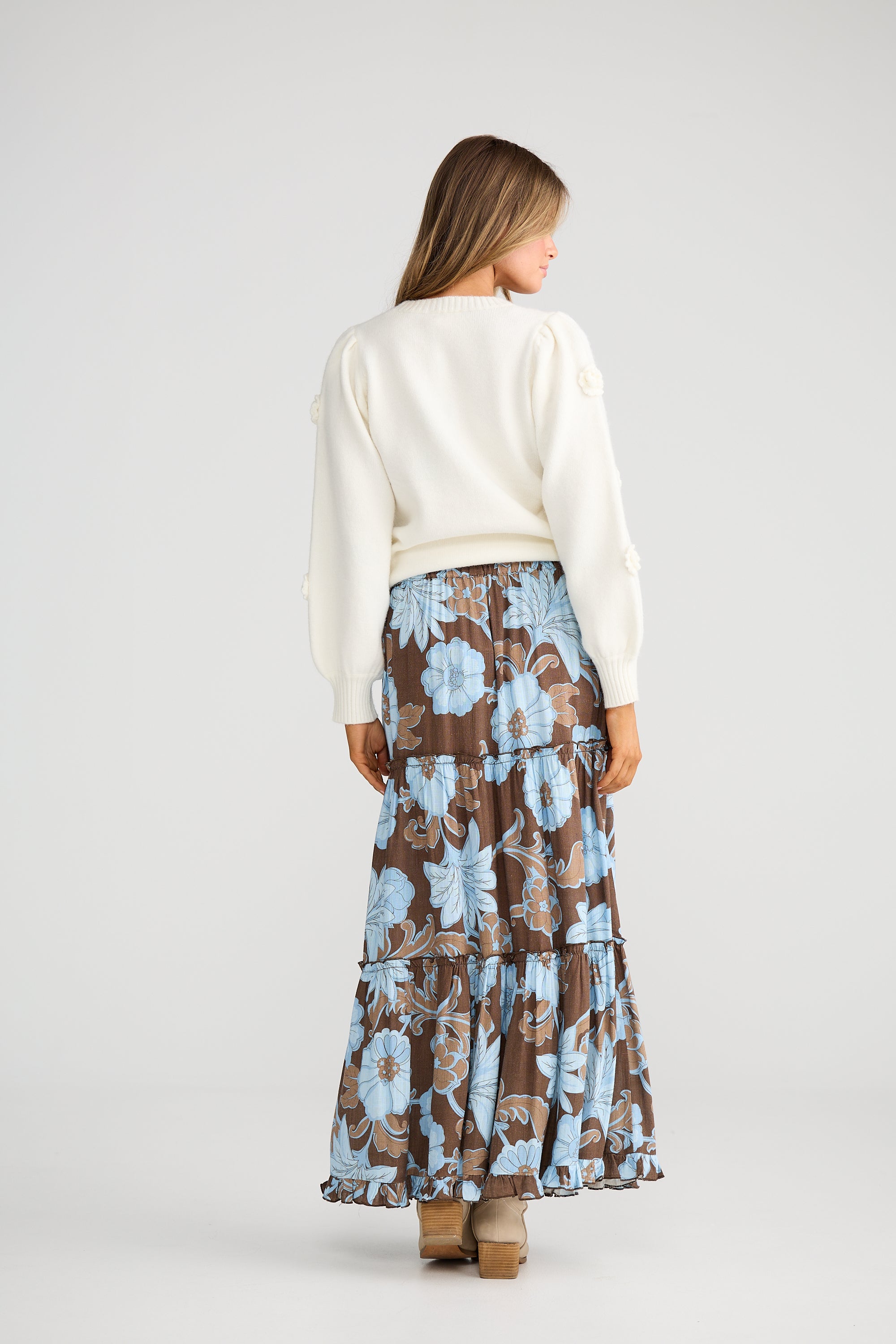 Collection of Woman wearing a Talisman white sweater and Talisman floral skirt on a plain background in a gallery layout