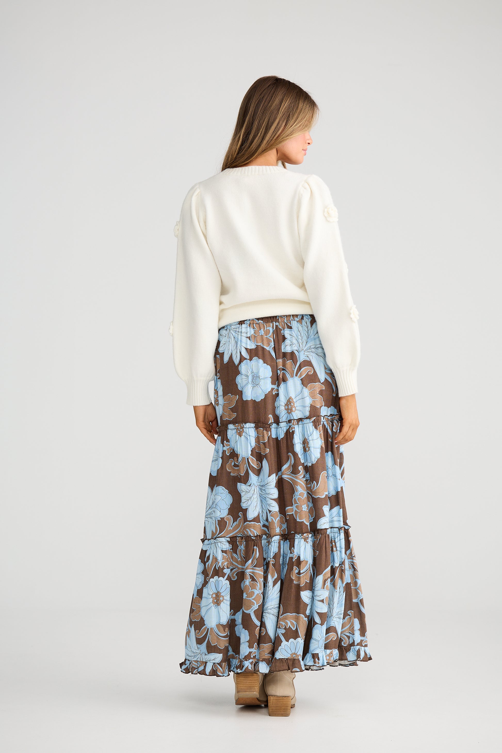Woman wearing a Talisman white sweater and Talisman floral skirt on a plain background