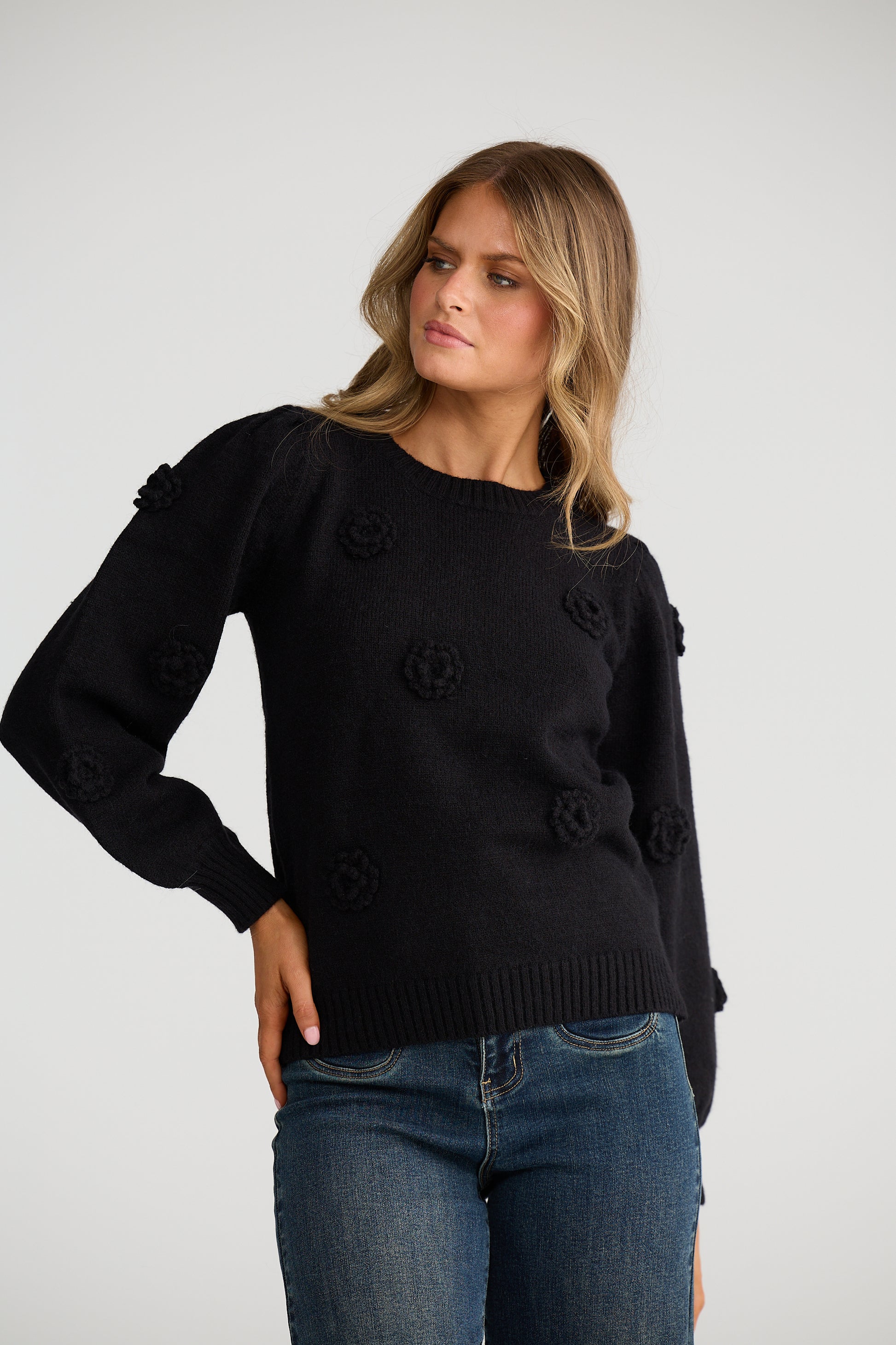 Woman wearing a Talisman black sweater with button details and blue jeans on a white background