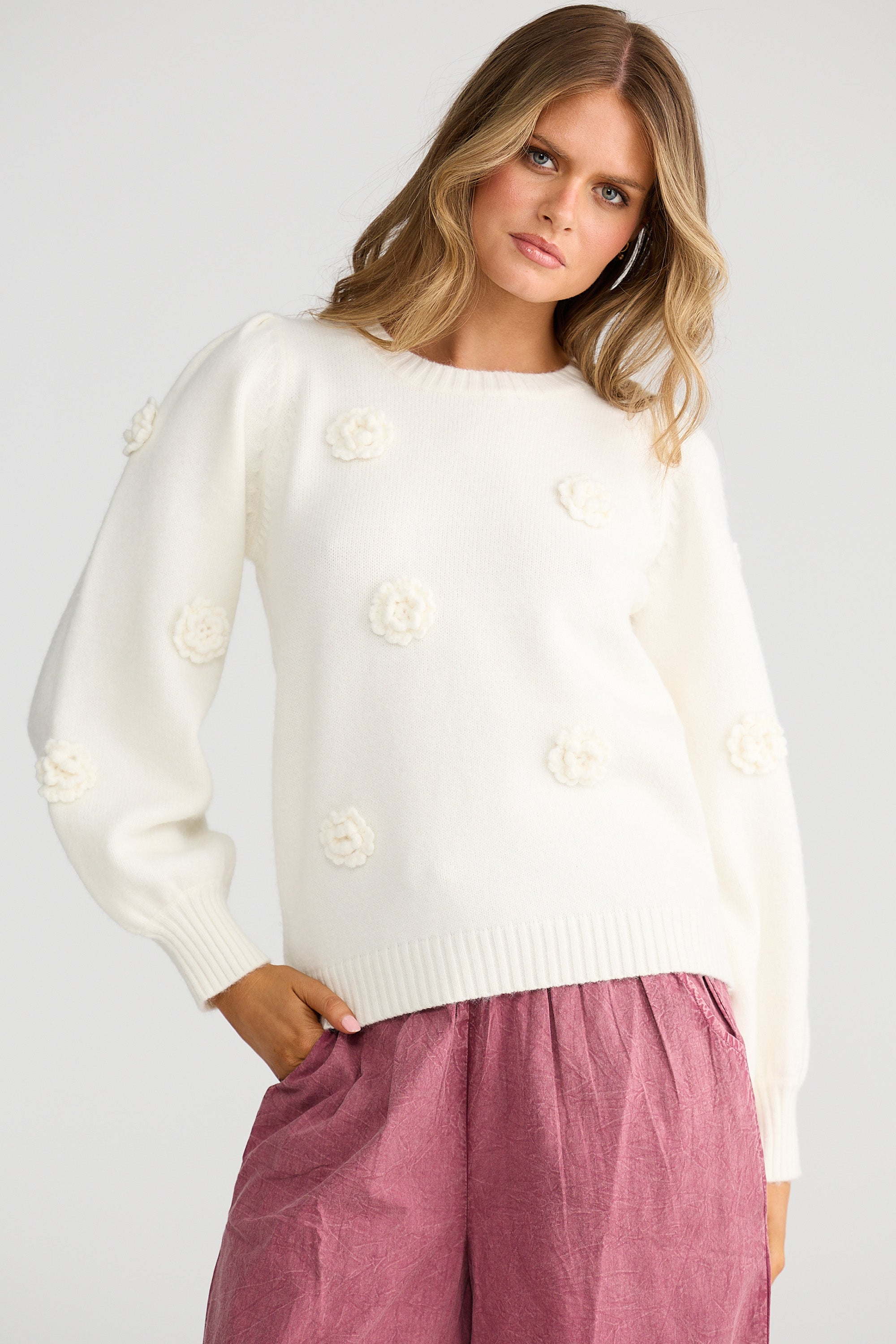 Collection of Woman wearing a Talisman white sweater with floral patterns and pink pants on a plain background in a gallery layout