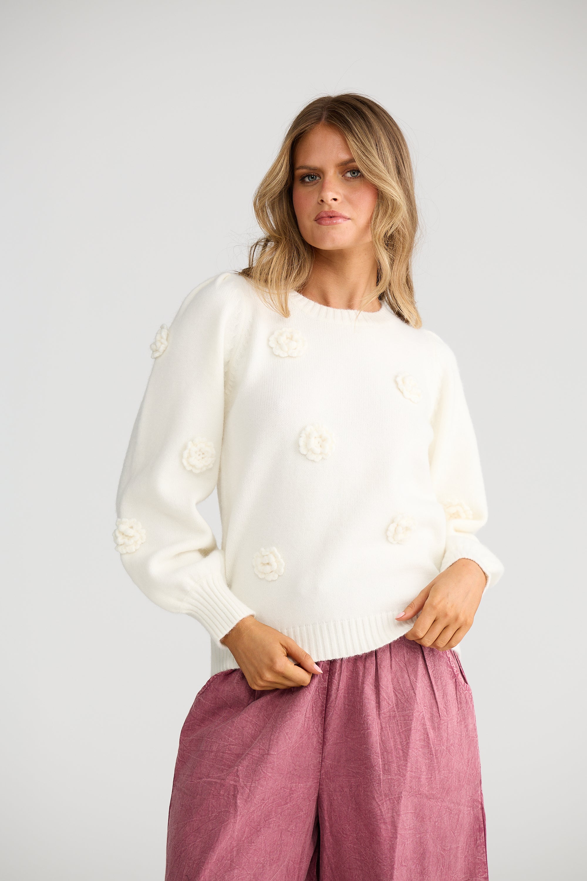 Collection of Woman wearing a Talisman white sweater with button details and pink pants on a plain background in a gallery layout