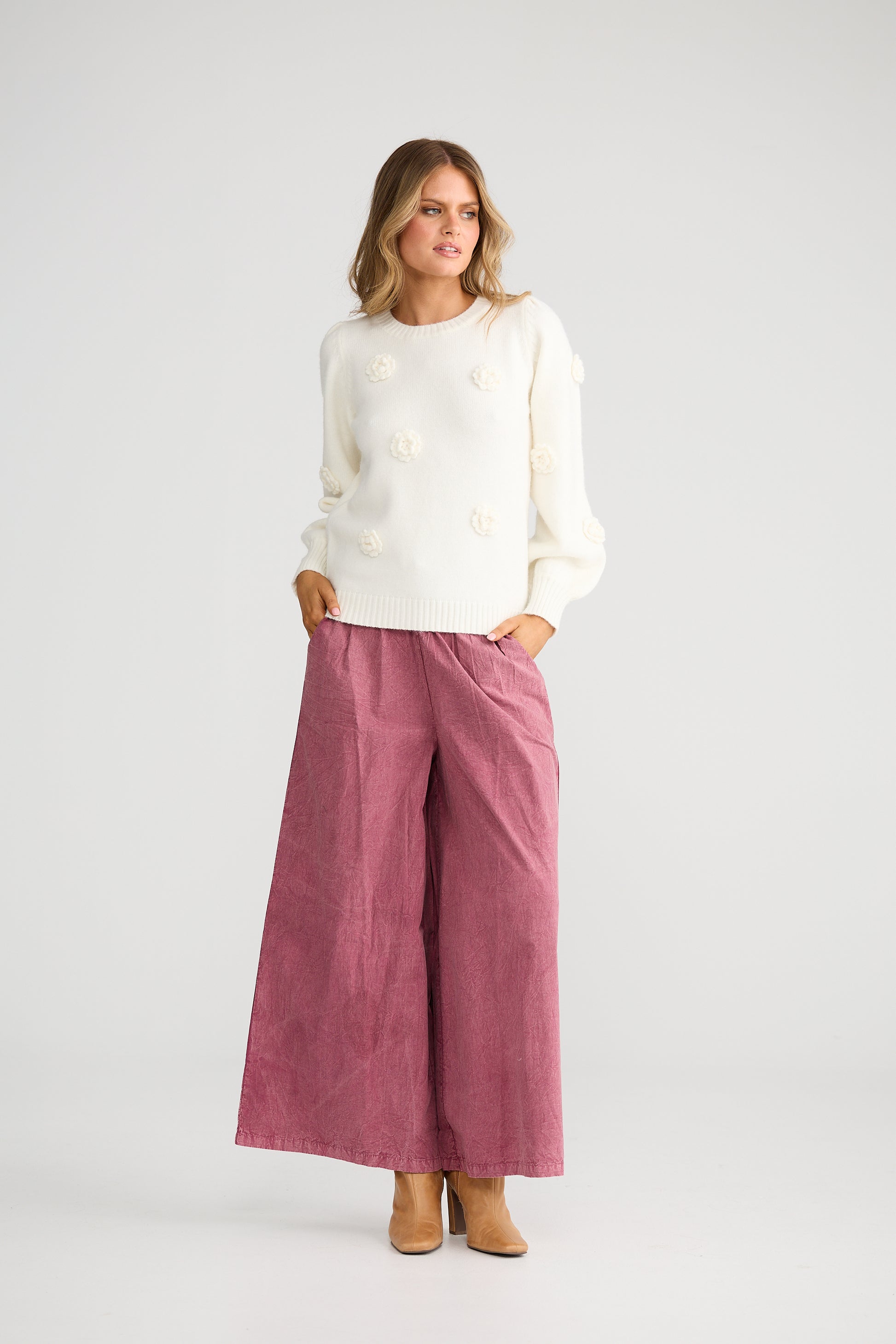 Woman wearing a Talisman white sweater and pink pants on a light gray background