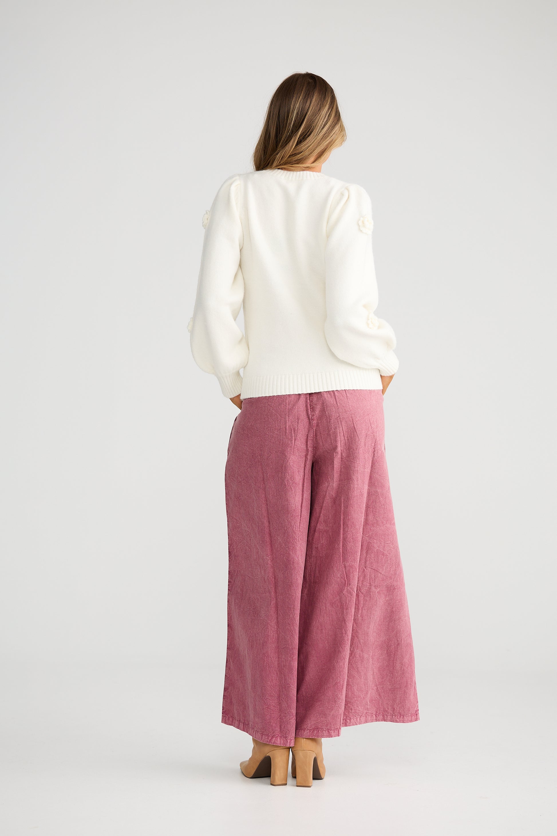 Woman wearing a Talisman white top and pink pants on a white background