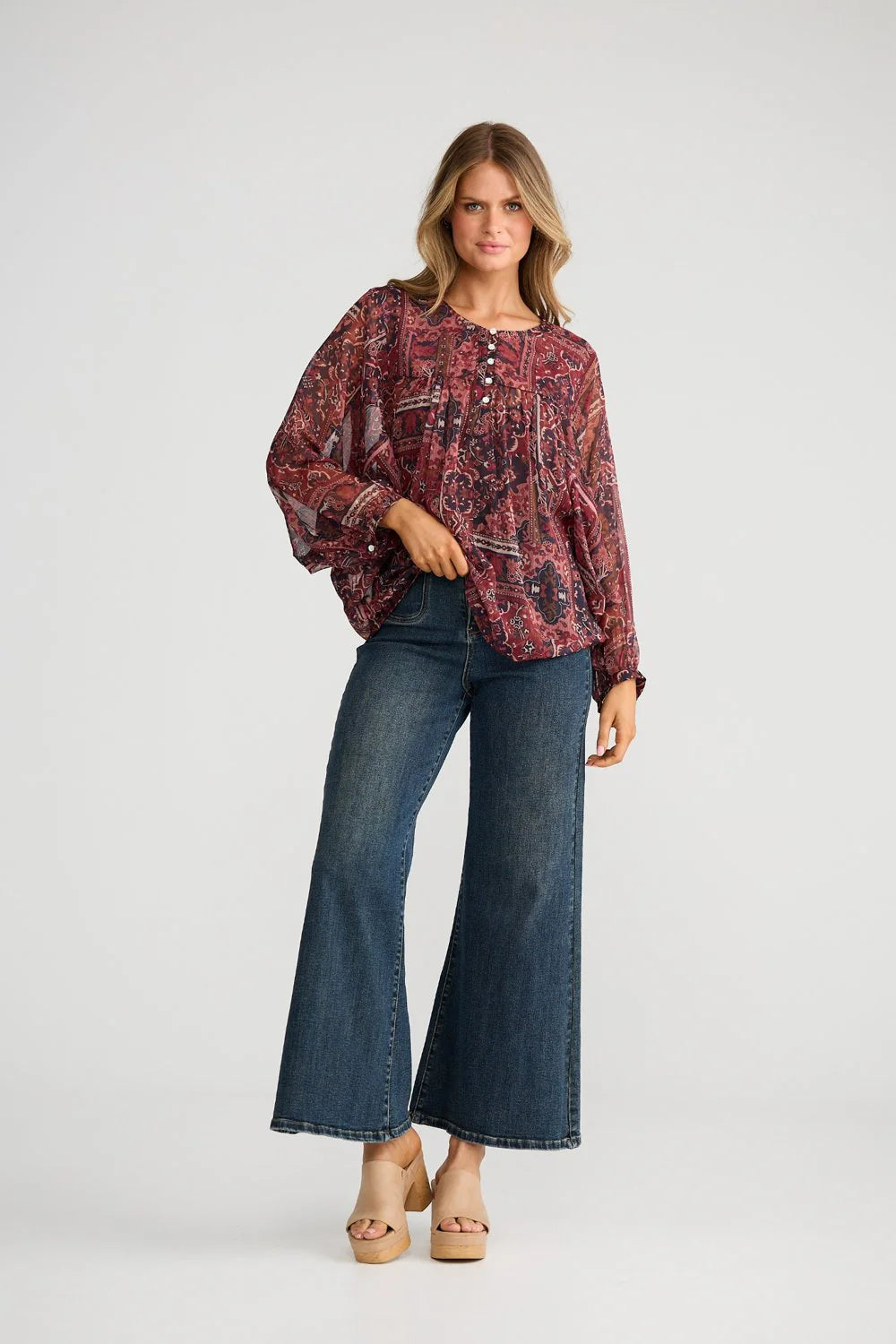 Woman wearing a Talisman patterned blouse and blue jeans on a white background