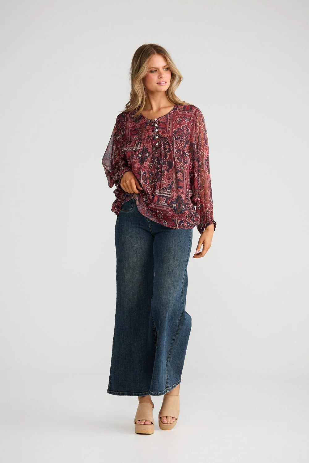 Image of Woman wearing a Talisman patterned blouse and blue jeans on a white background