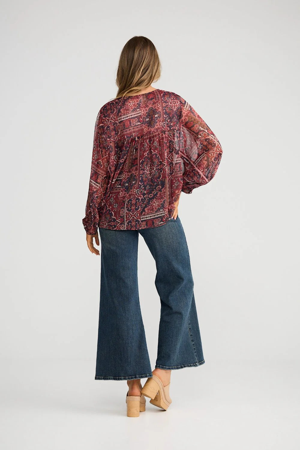 Woman wearing a Talisman patterned blouse and blue jeans on a white background