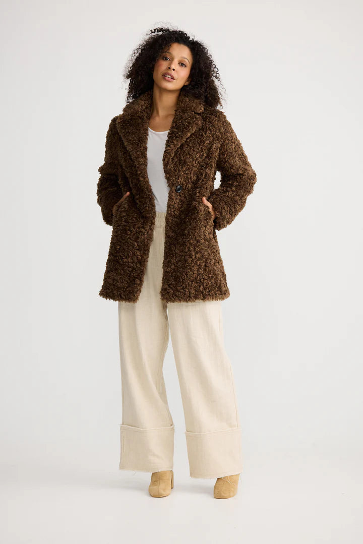 Image of Woman wearing a Shanty Corporation brown textured coat with white pants on a light background