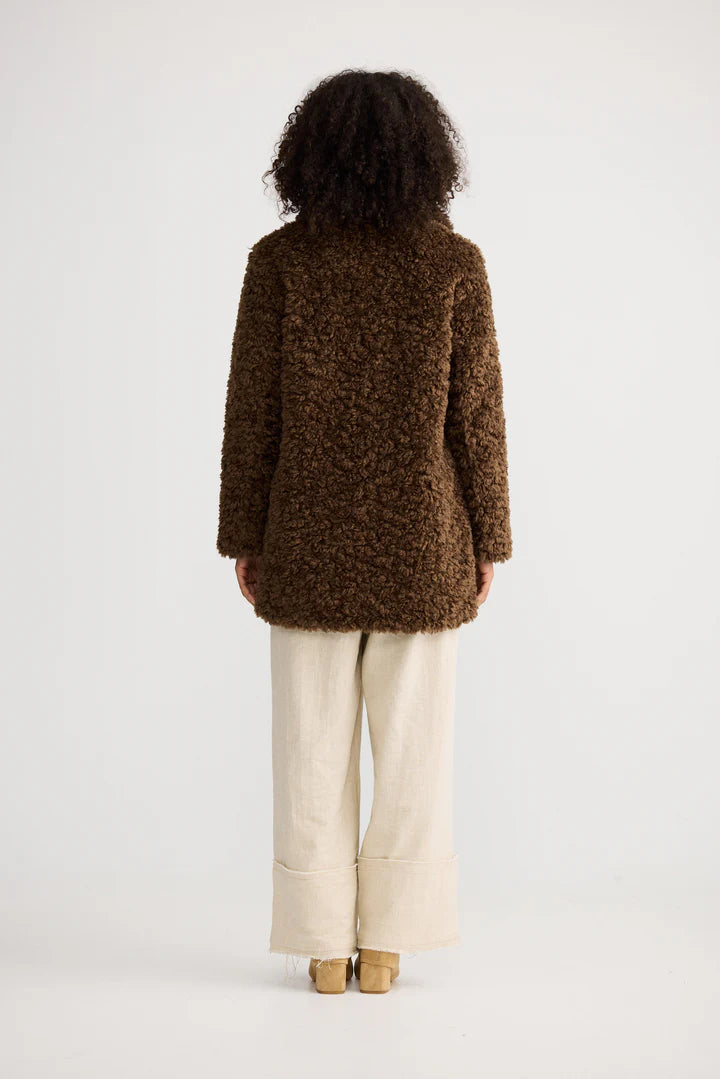 Image of Person wearing a Shanty Corporation brown textured coat and beige pants on a white background